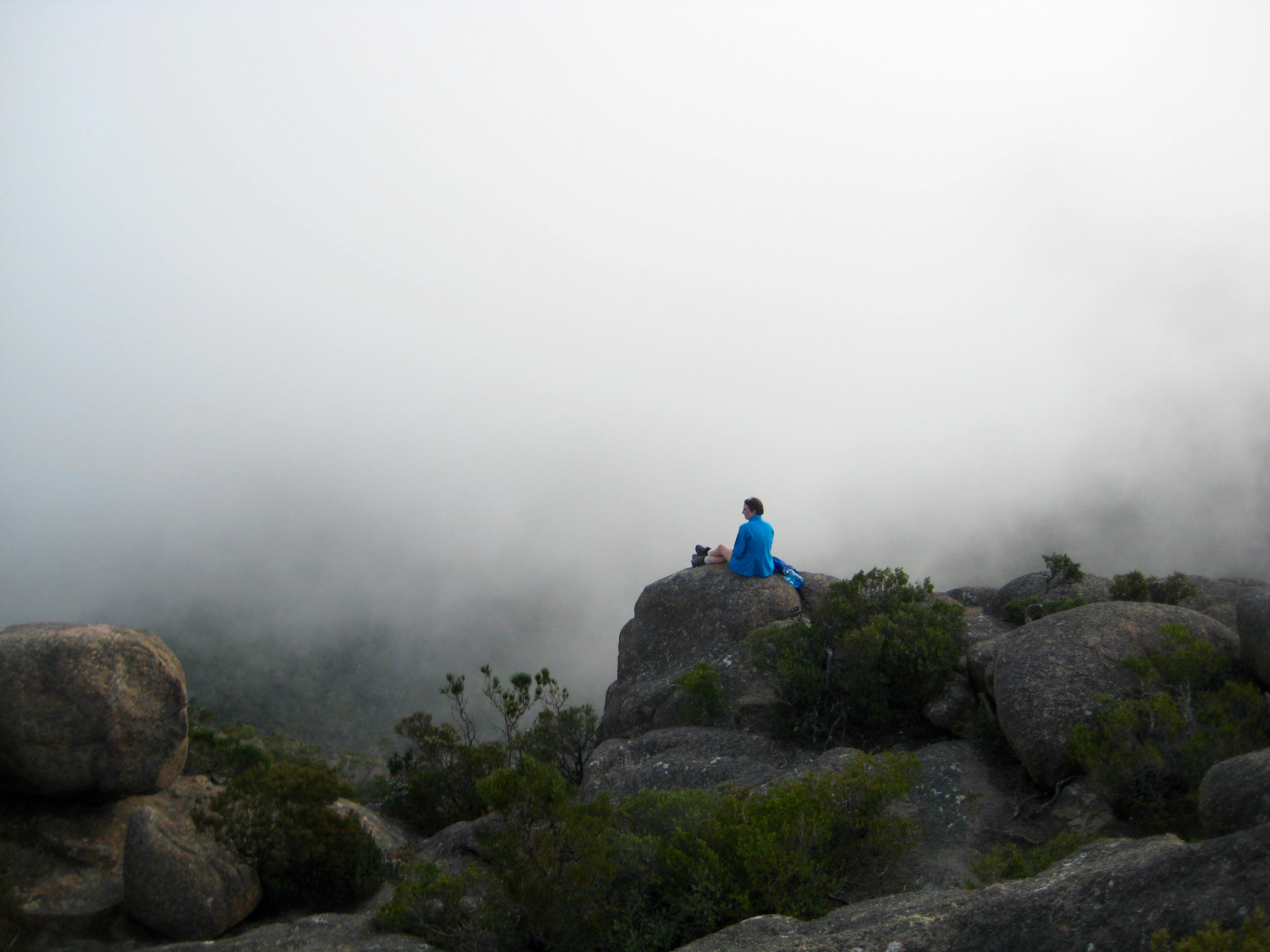 hiker sitting on rock slab in the clouds on the summit of Mt Amos in Tasmania's Freycinet National Park