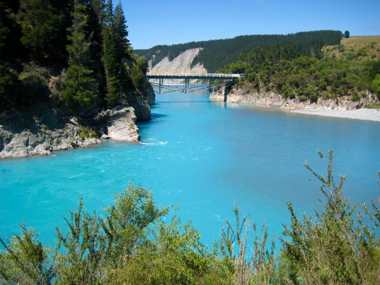A turquoise river flows down a valley toward a bridge