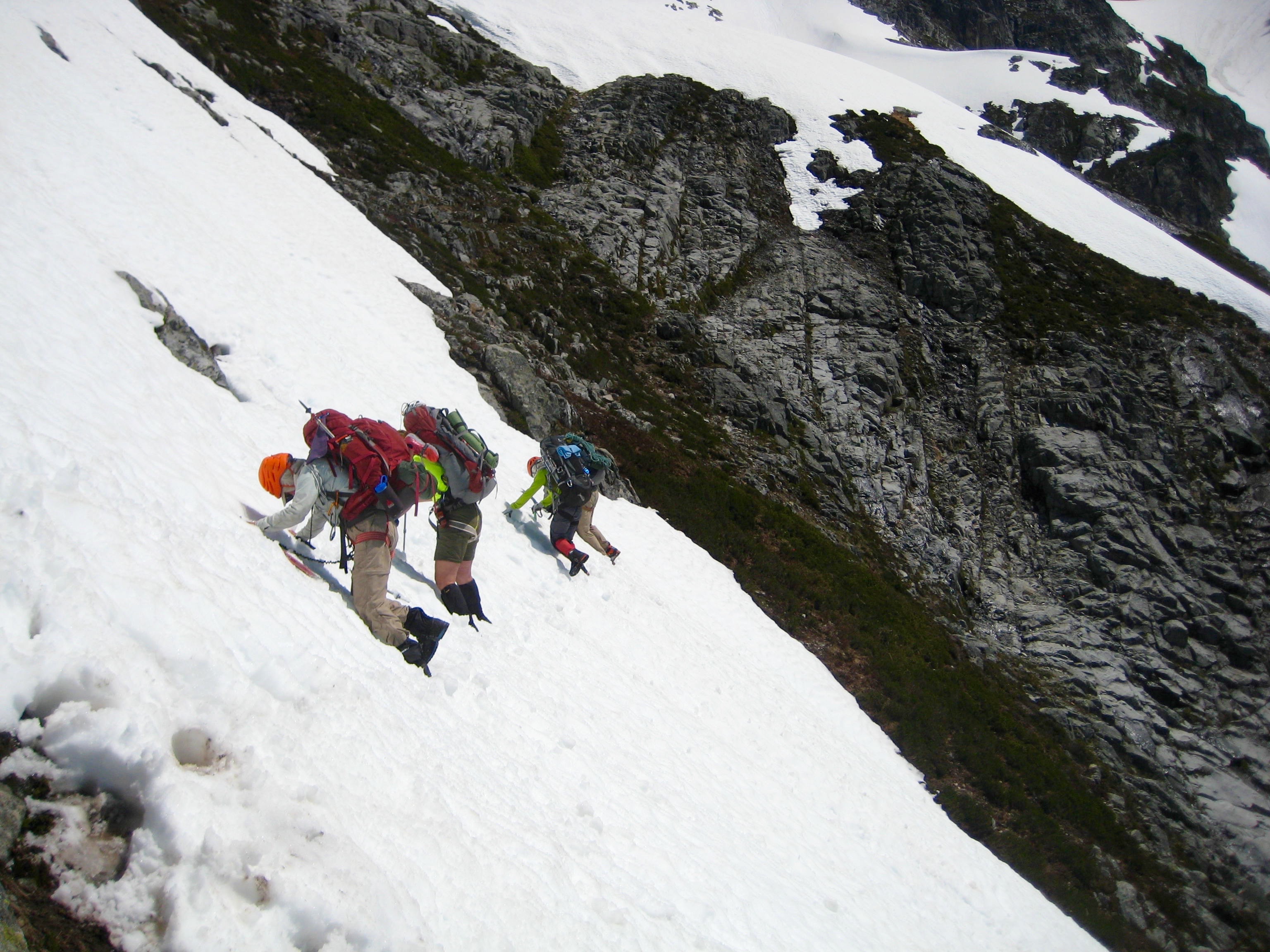 climbers traverse steep snow leading down from Pickell Pass