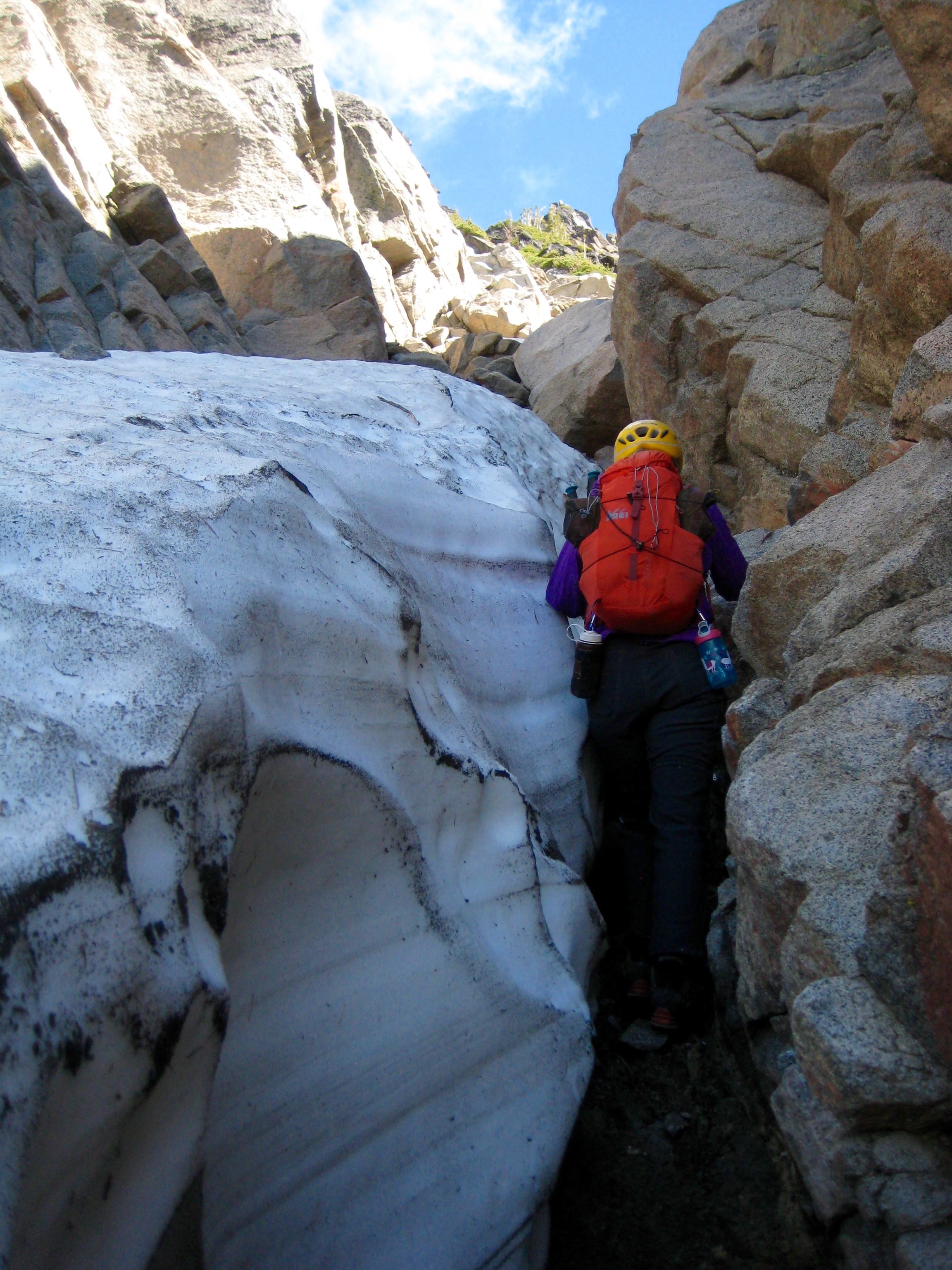 mountain climber squeezing between snow and steep rock side of southeast gully on Sherpa Peak in the Icicle Mountains