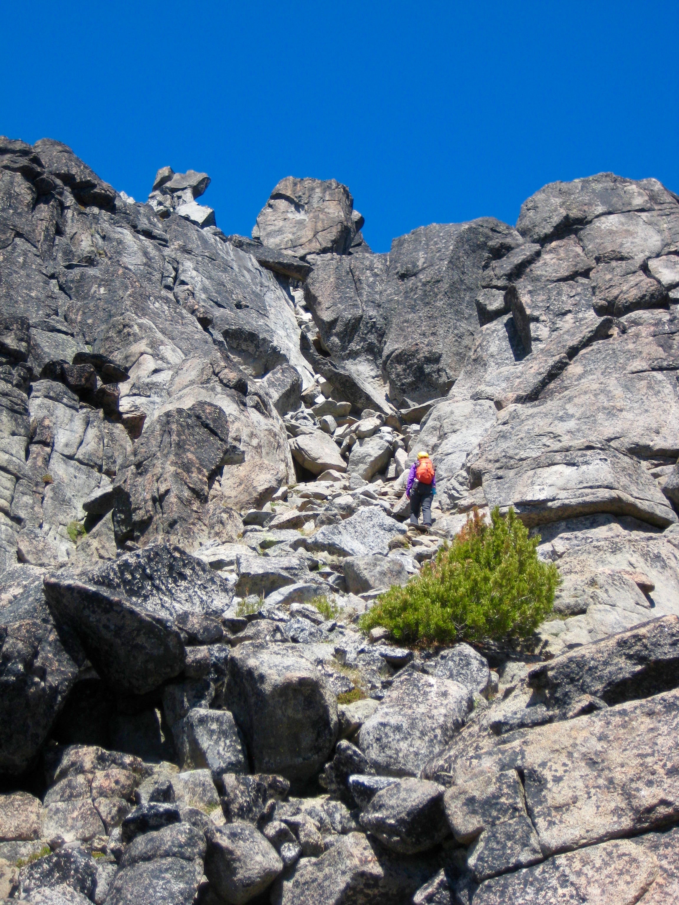mountain climber scrambling large boulders in a rocky slot high on Sherpa Peak in the Icicle Mountains