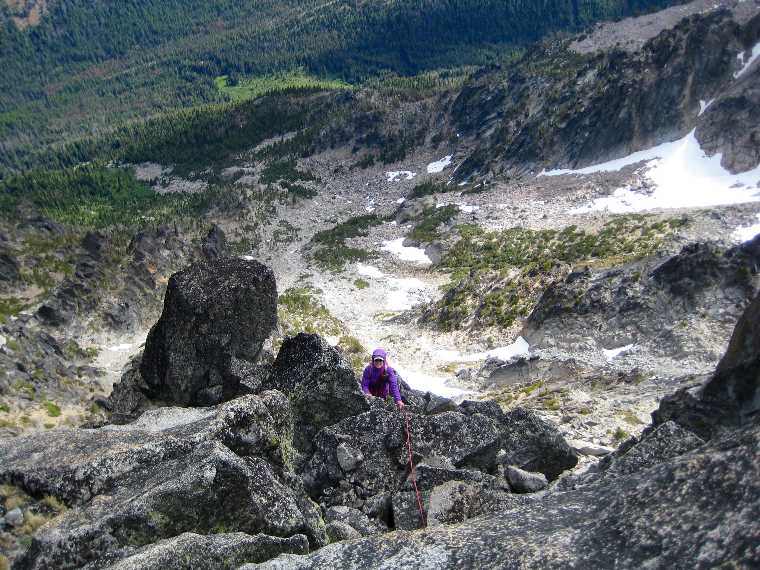 looking down on mountain climber scrambling south ridge on Sherpa Peak with rocky basin and snow patches in the background 