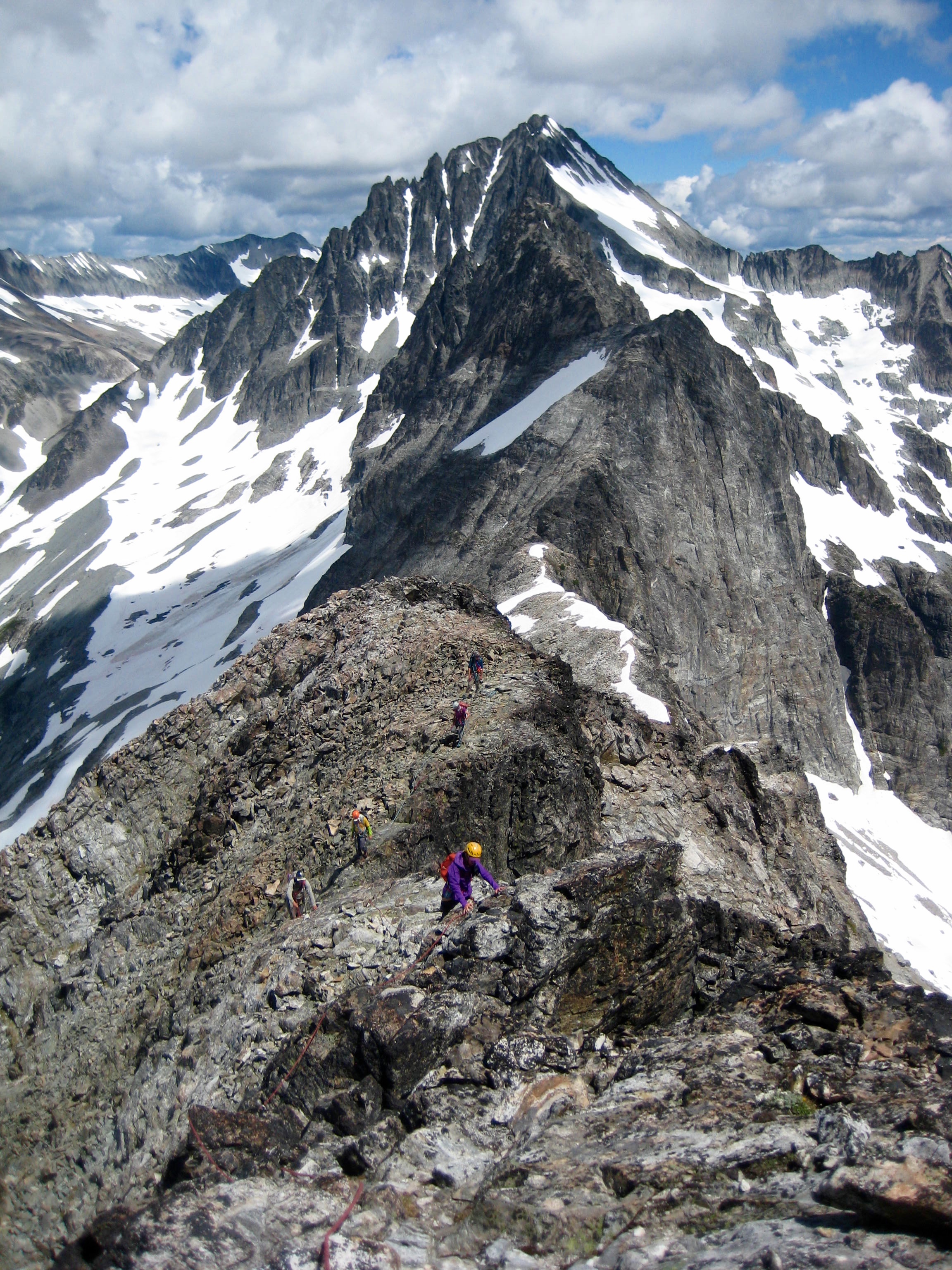 roped mountain climbers scrambling steep rocky ridge of Easy Mox Peak in the American Chilliwack Mountains with Mt Spickard in the background