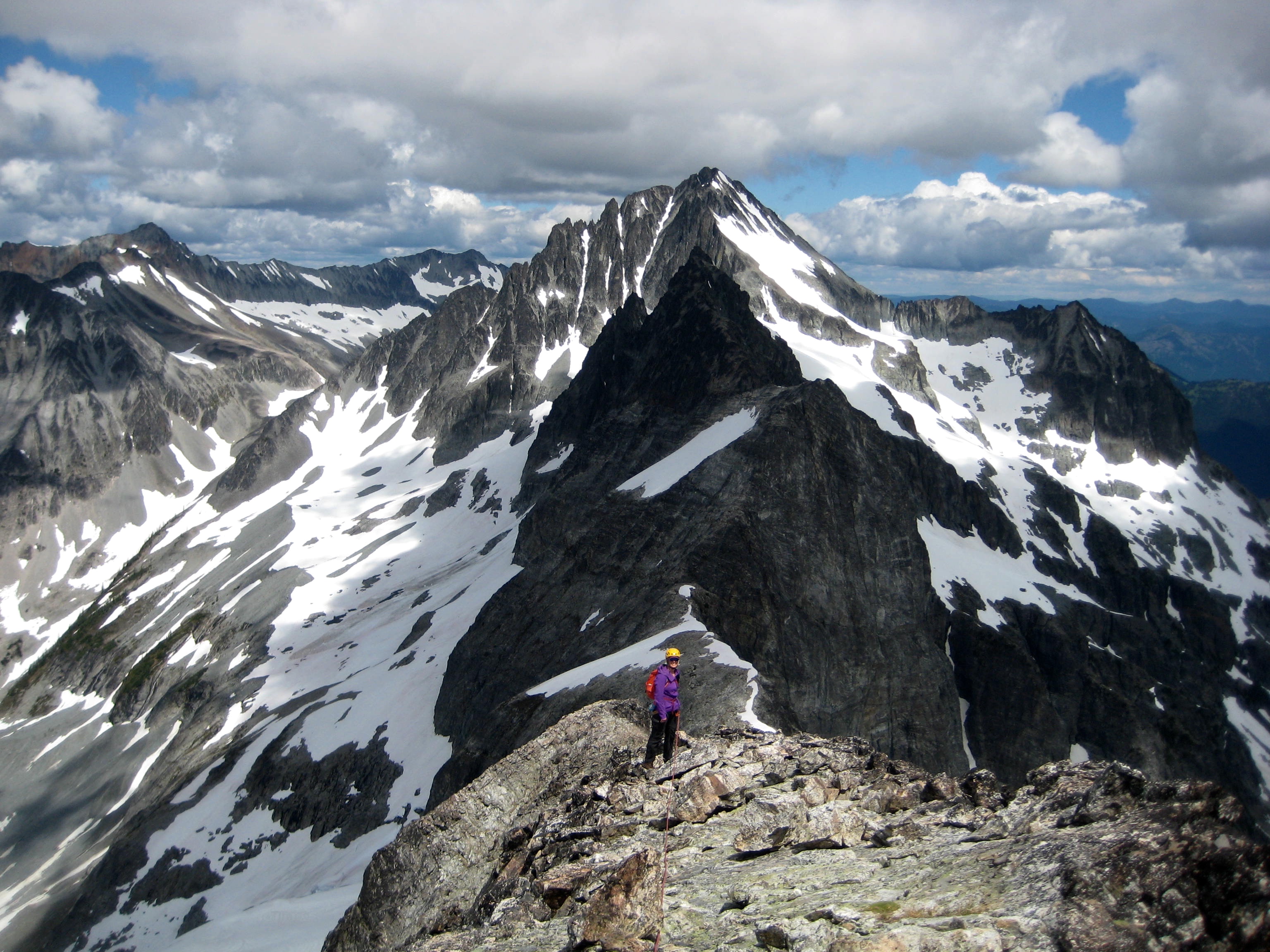Mountain climber scrambling on Upper Easy Mox Ridge with Mt Spickard in the background
