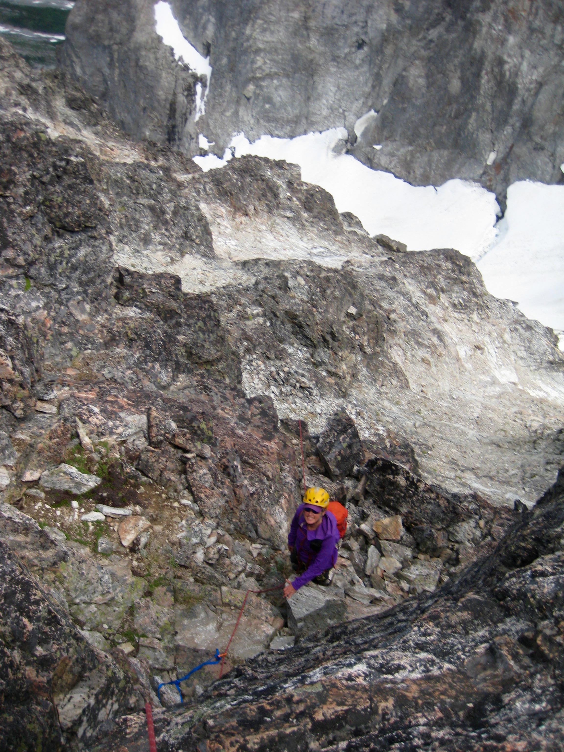 looking down on roped mountain climber scrambling the loose rock boulders on the summit tower of Easy Mox Peak in the American Chilliwack Mountains with snow field below