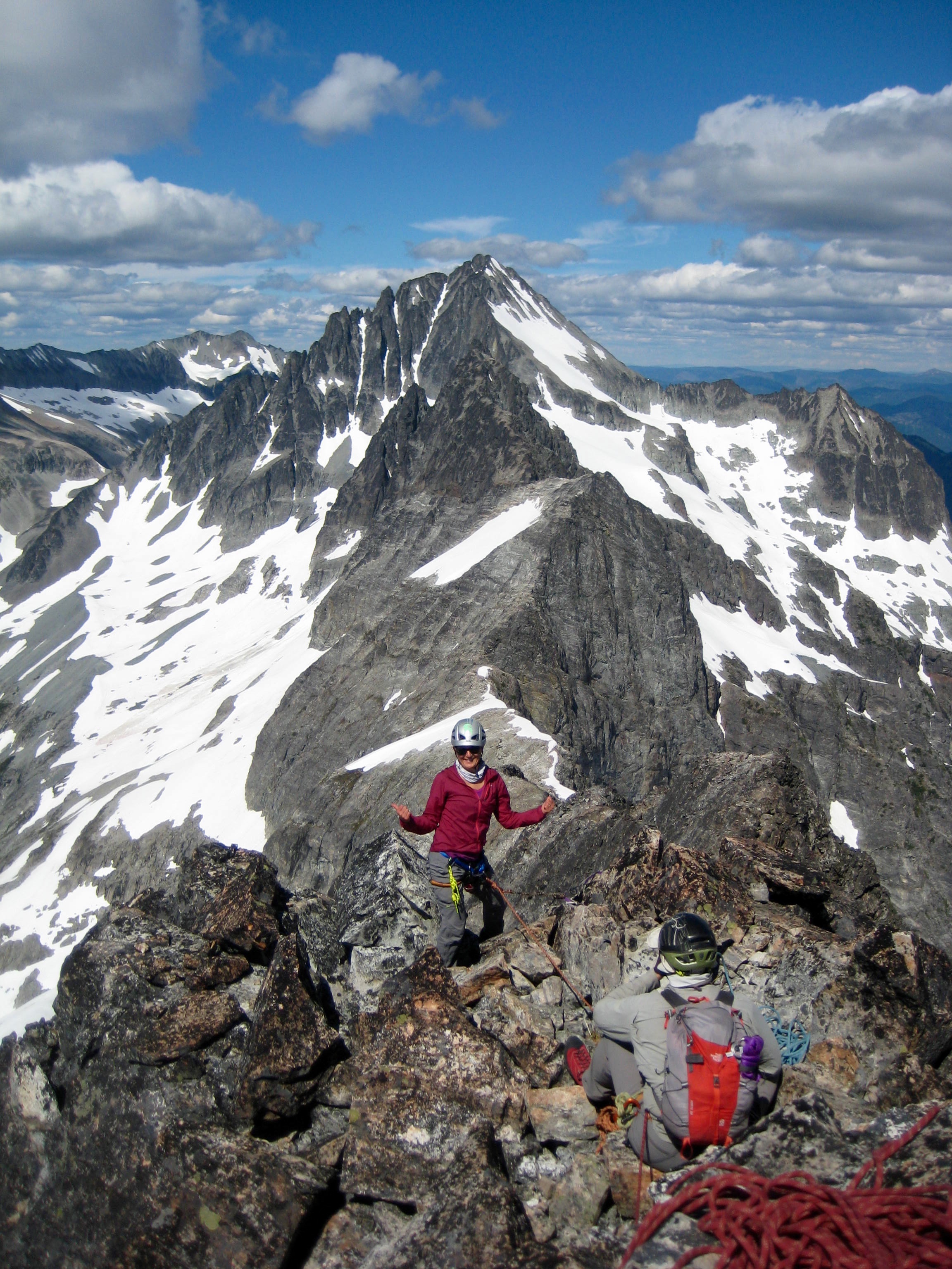 mountain climbers taking a break on the rocky summit of Easy Mox Peak in the American Chilliwack Mountains with Mt Spickard in the background