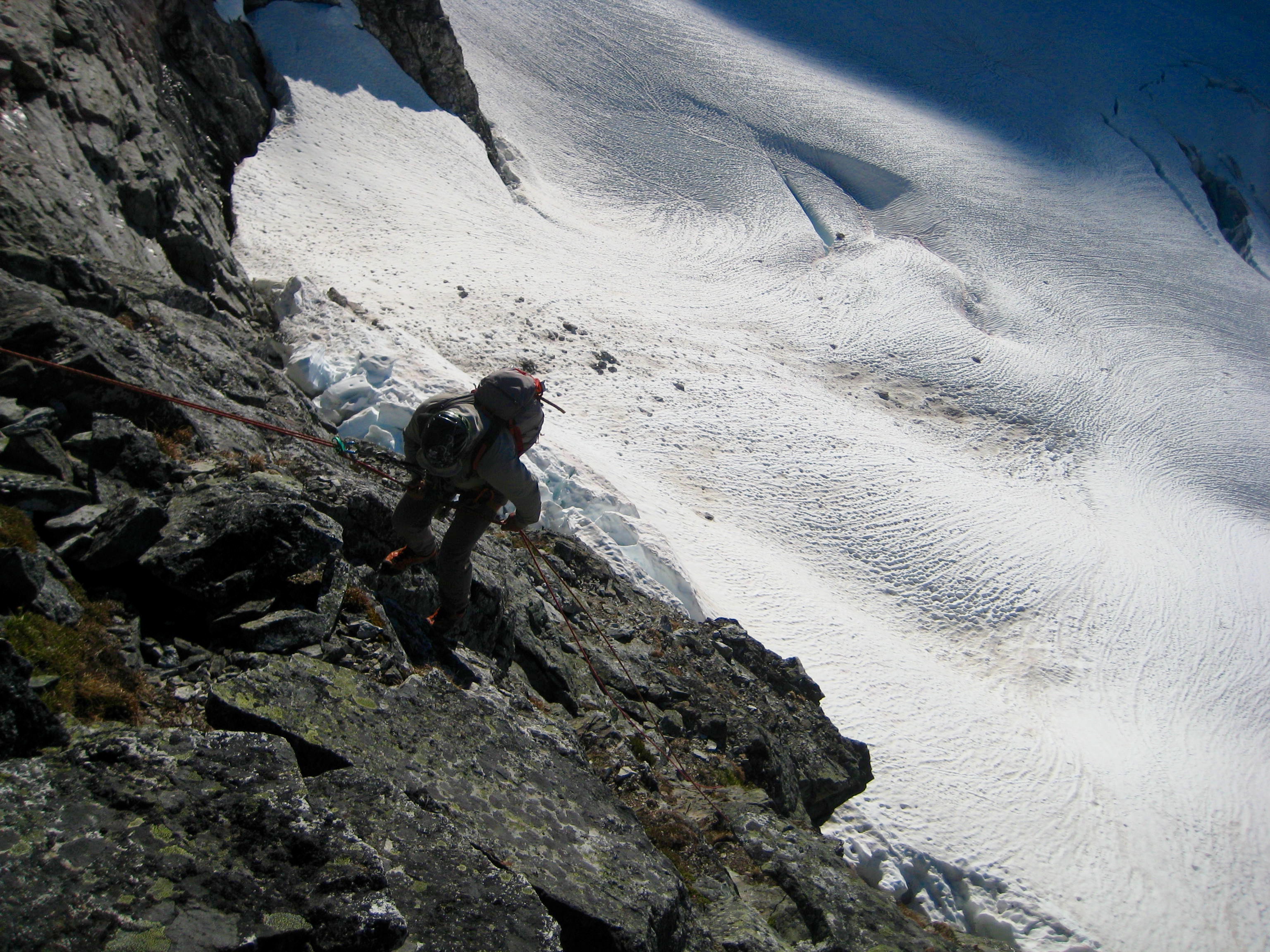looking down on mountain climber rappeling loose rock face on Easy Mox Peak in the American Chilliwack Mountains with Redoubt Glacier below
