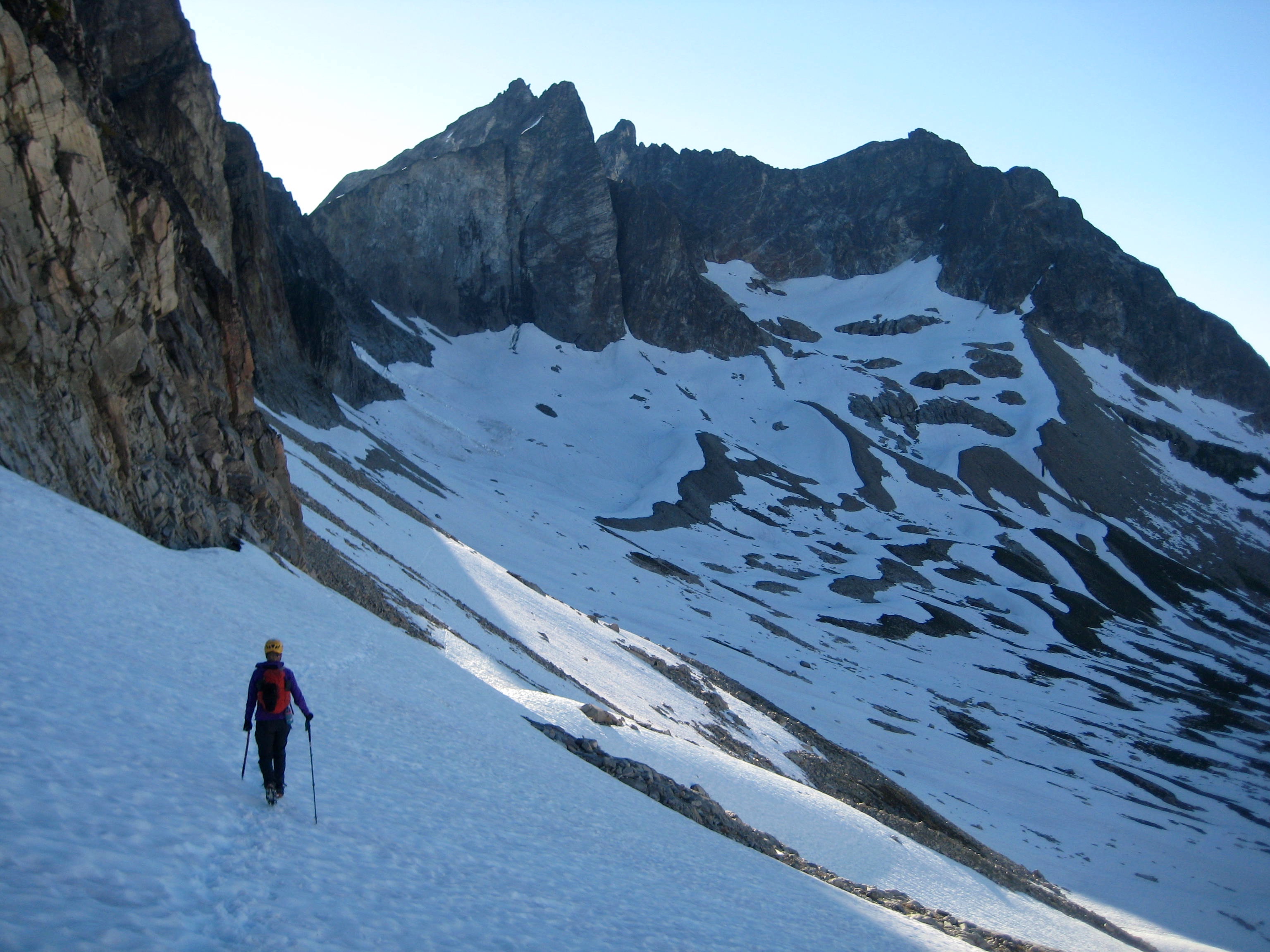 mountain climber traversing snow field in early morning light with Hard Mox Peak in the American Chilliwack Mountains in the distance