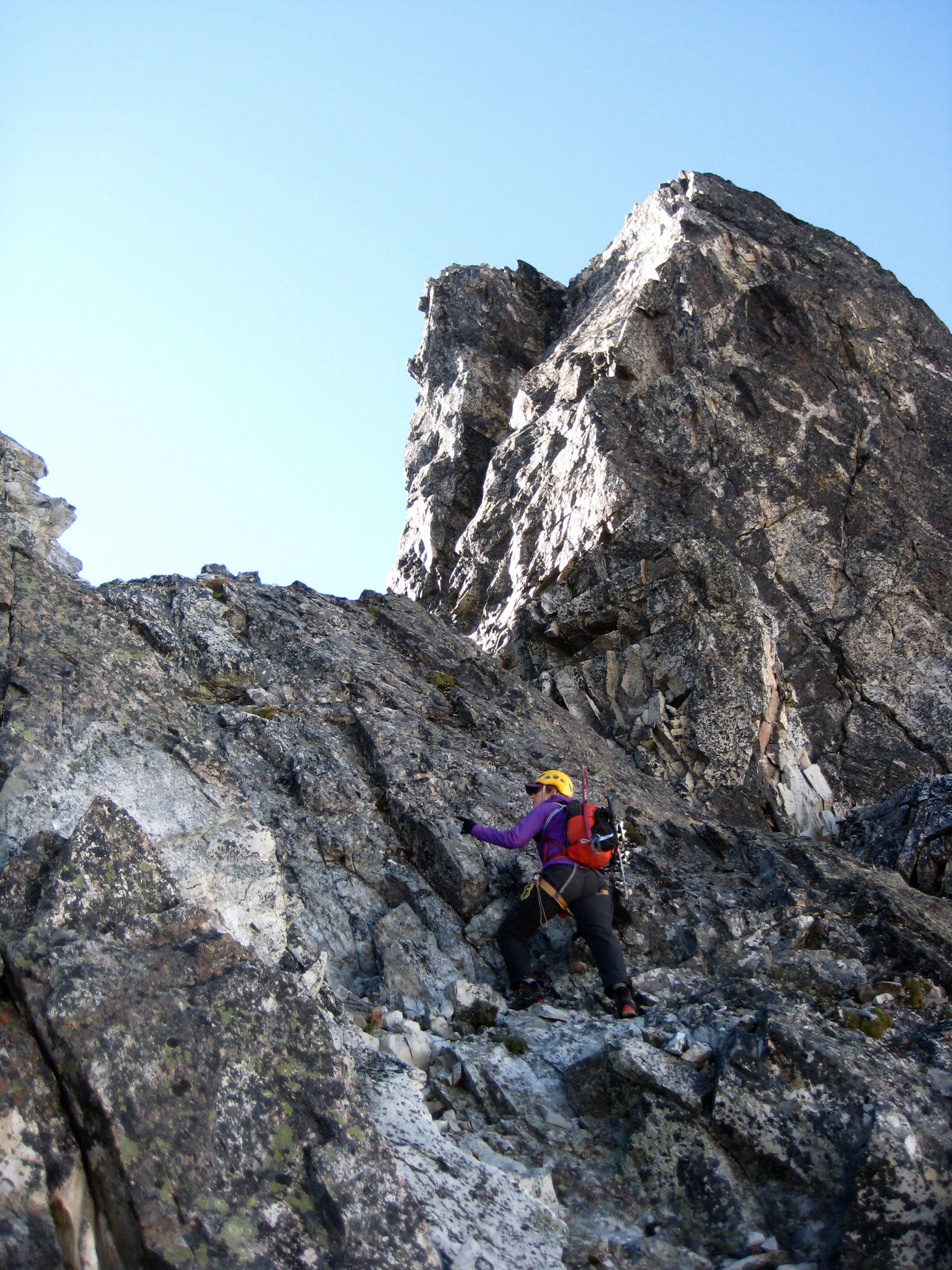 mountain climber scrambling up steep rock towards low spot on the ridge of the Gendarme in the American Chilliwack Mountains