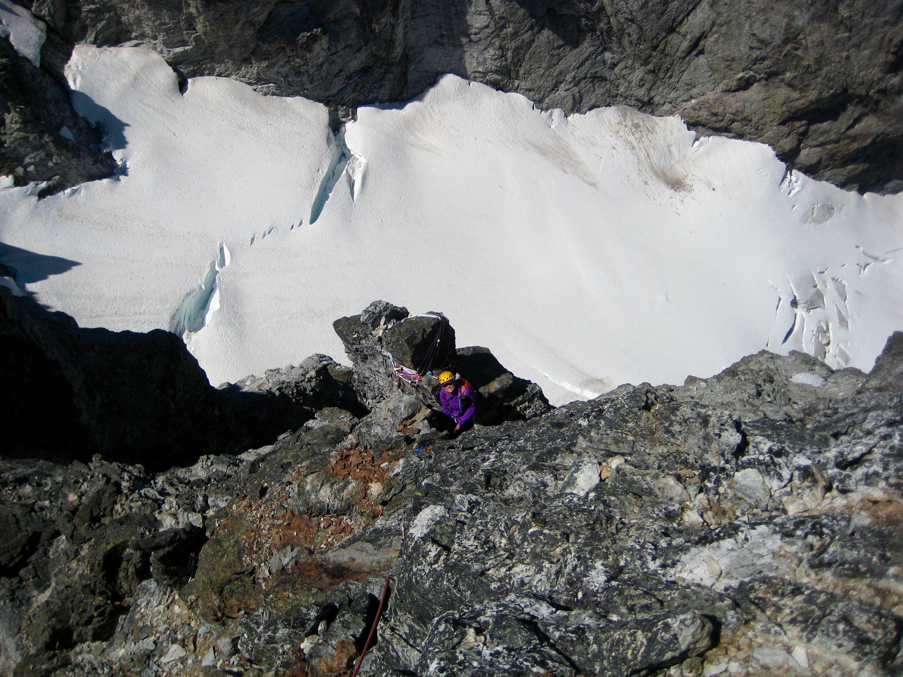 Looking down on Mountain climber belaying and snow patch on second summit rock pitch of Hard Mox Peak