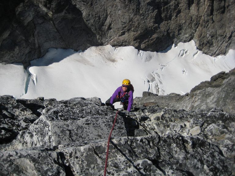 Looking down on a roped mountain climber ascending vertical cliff on second summit pitch on Hard Mox Peak in teh American Chilliwack Mountains