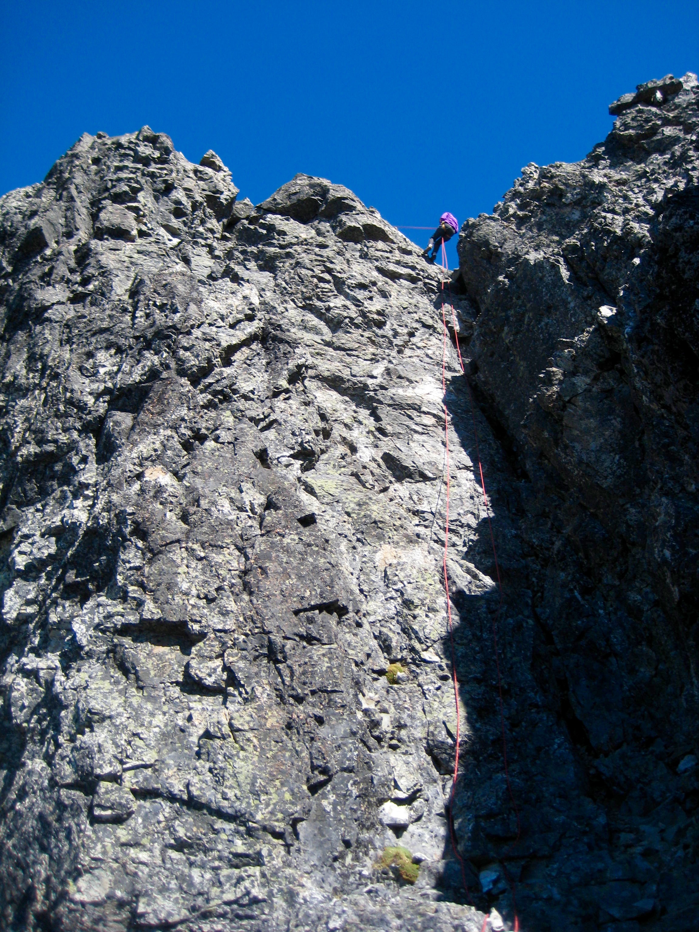 looking up at mountain climber rappelling vertical rock summit tower of Hard Mox Peak in the American Chilliwack Mountains