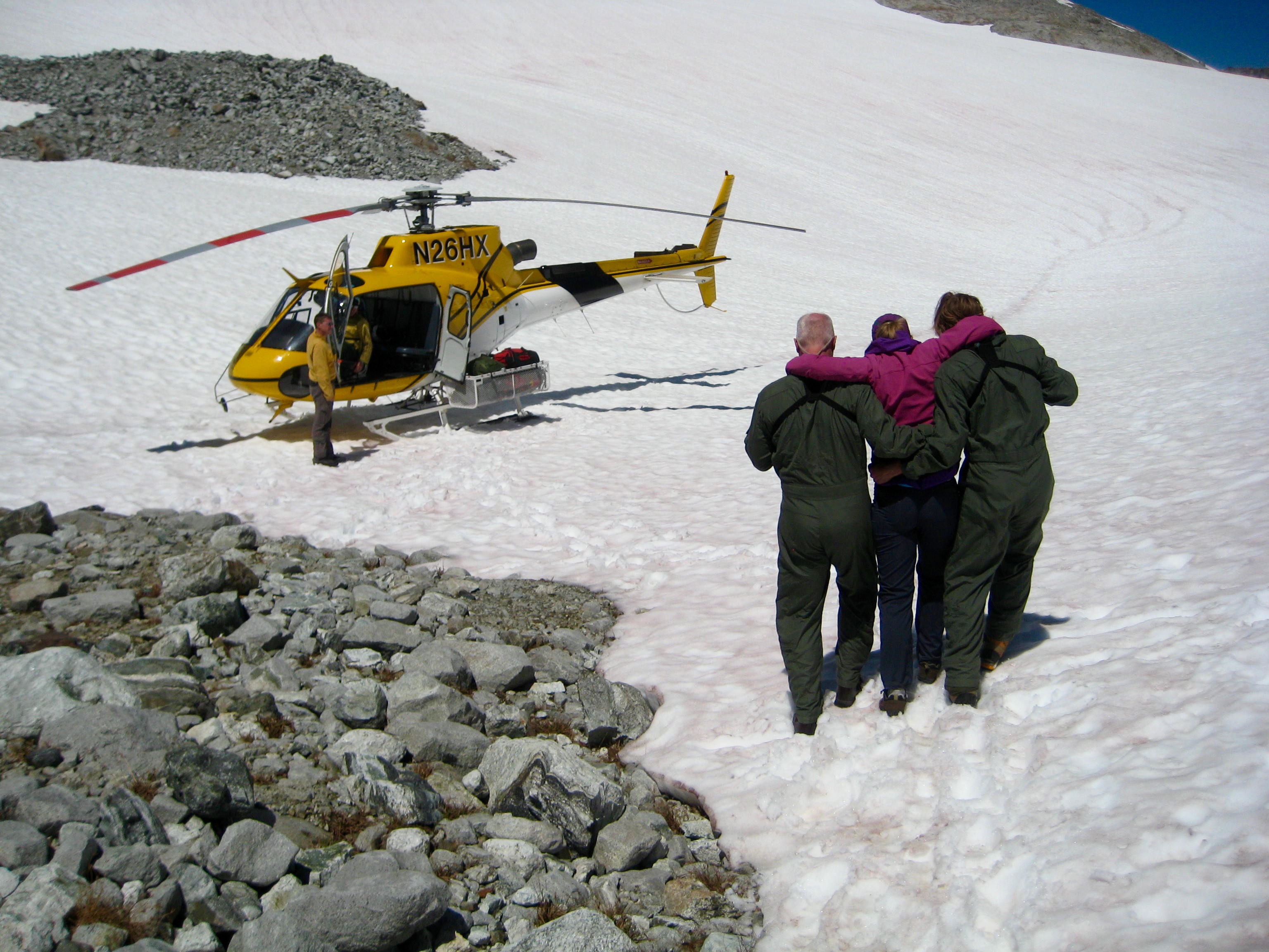 injuried mountain climber with mountain rescue rangers assistance crossing Redoubt Glacier heading toward rescue helicopter in the American Chilliwack Mountains