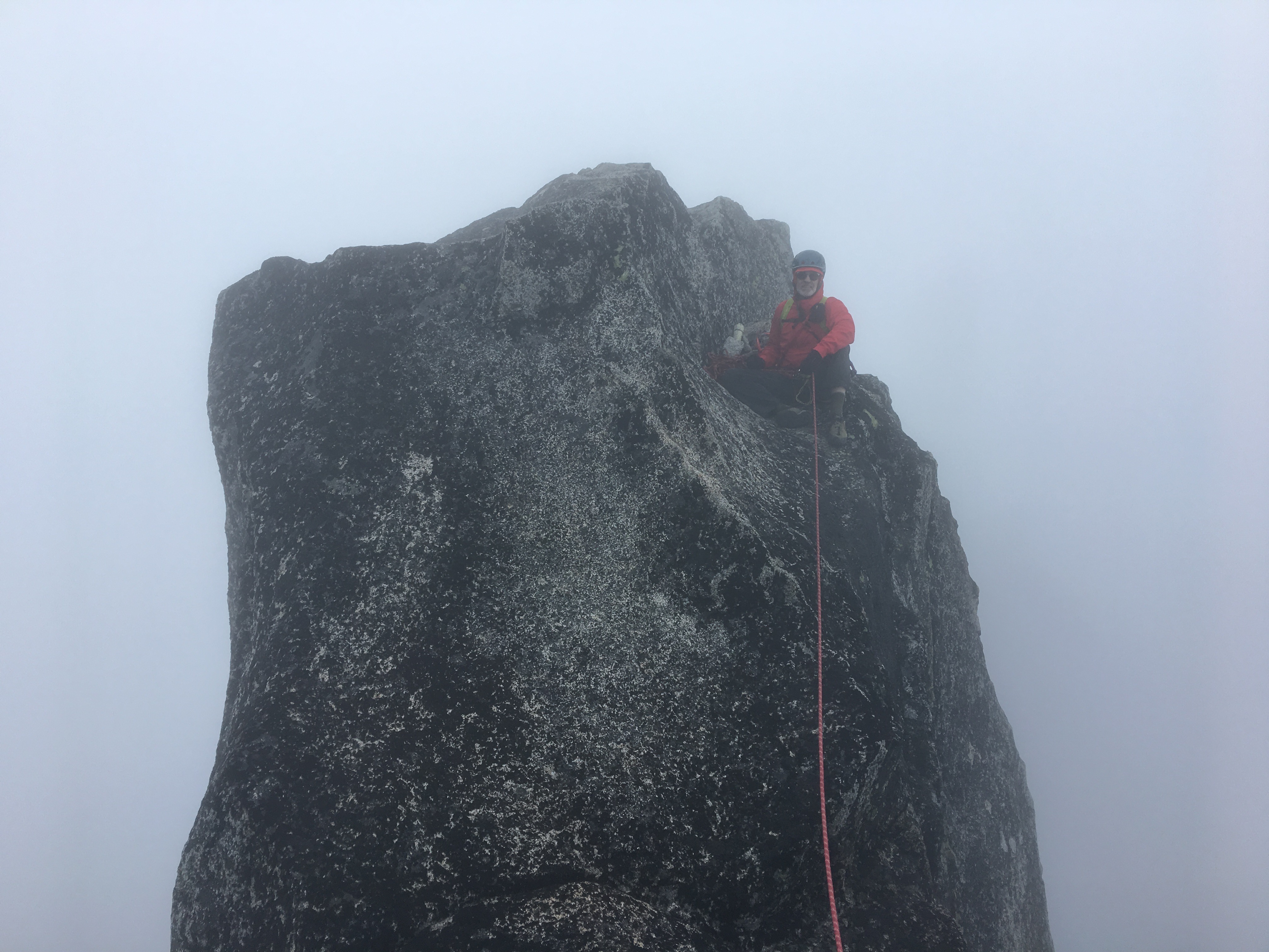 roped mountain climber belaying from the summit of Sherpa Peak in the fog in the Alpine Lakes Wilderness