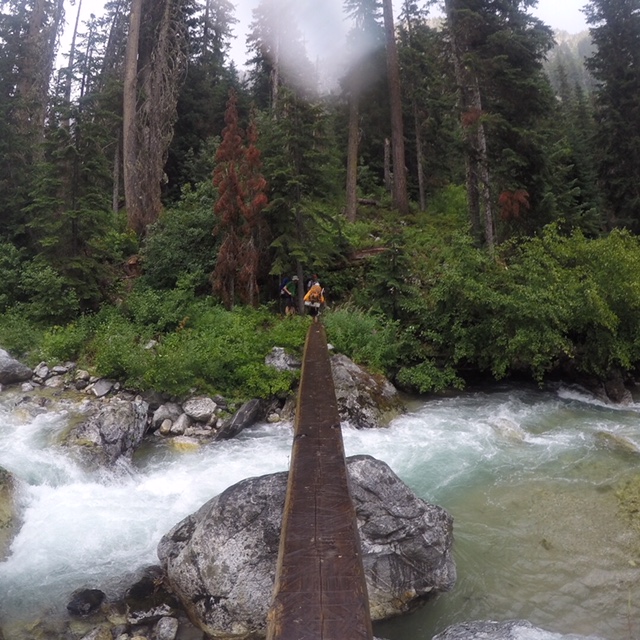 mountain climber on very narrow wood lodge bridge over Park Creek in the North Cascades enroute to Mt Logan