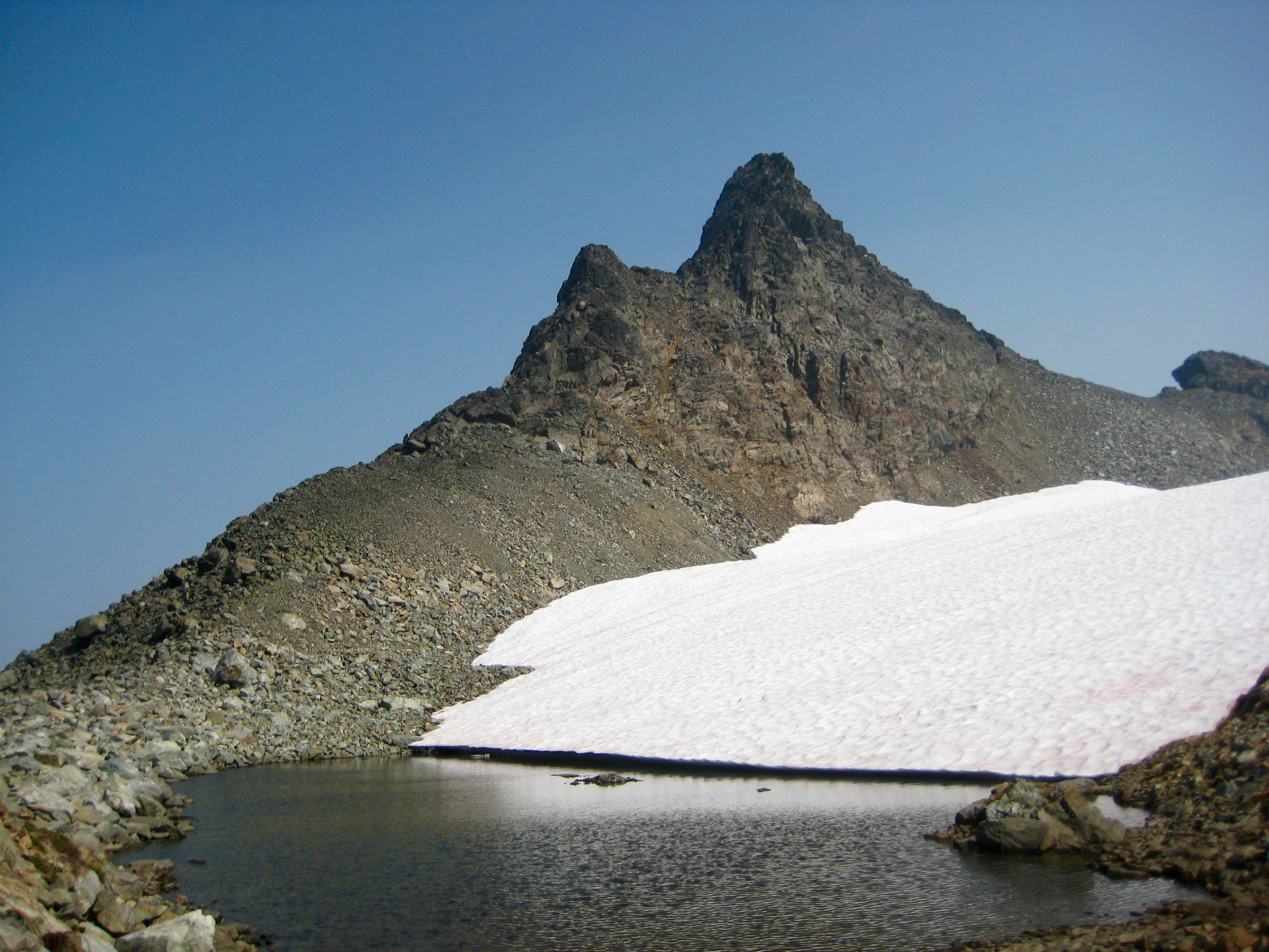rock, horn pinnacle shaped Stewart Peak in the Cheam Range with large snow field and melted out tarn
