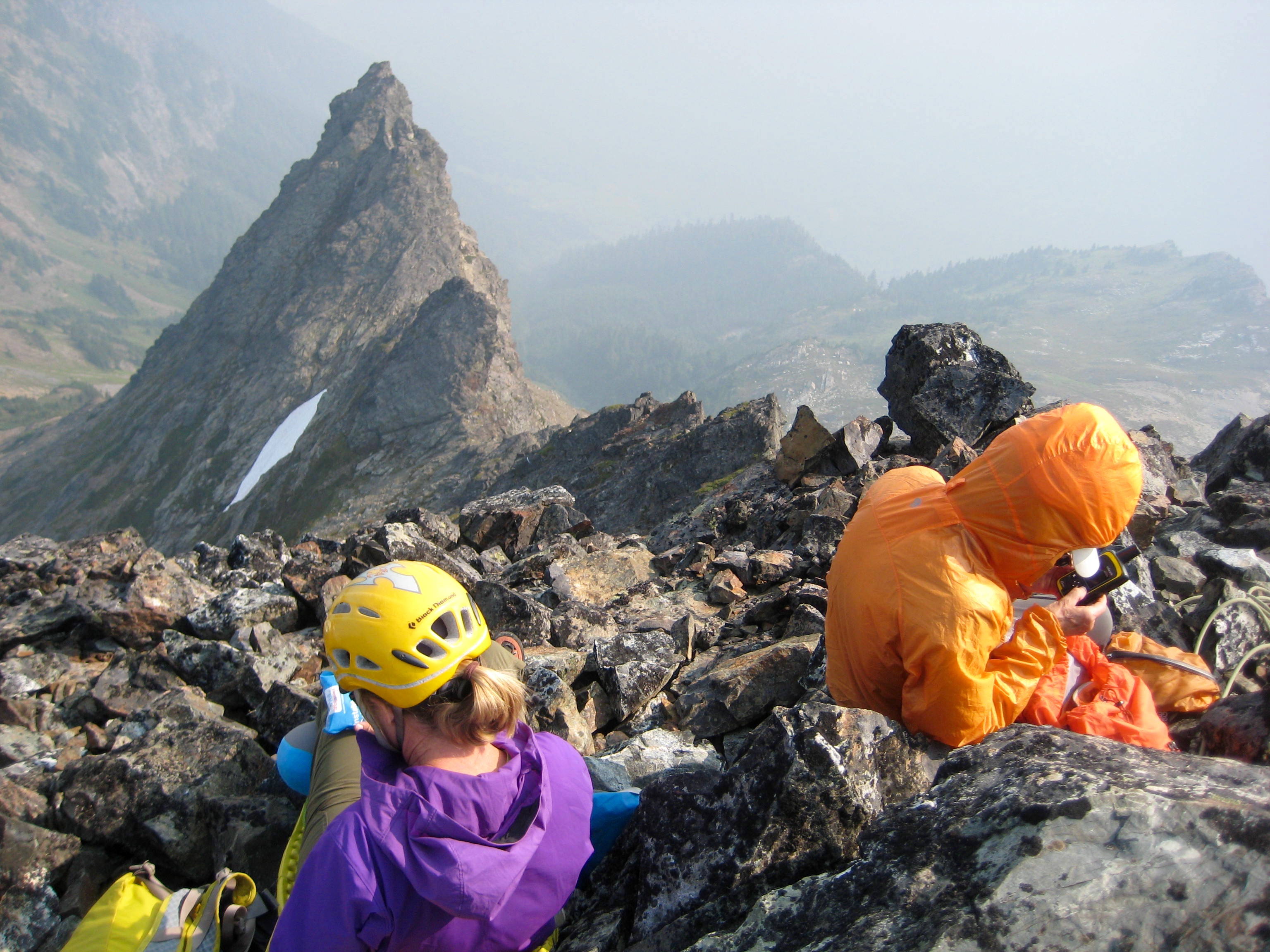 mountain climbers taking a break on the summit of Baby Munday Peak in the Cheam Range looking down the steep, rocky south ridge