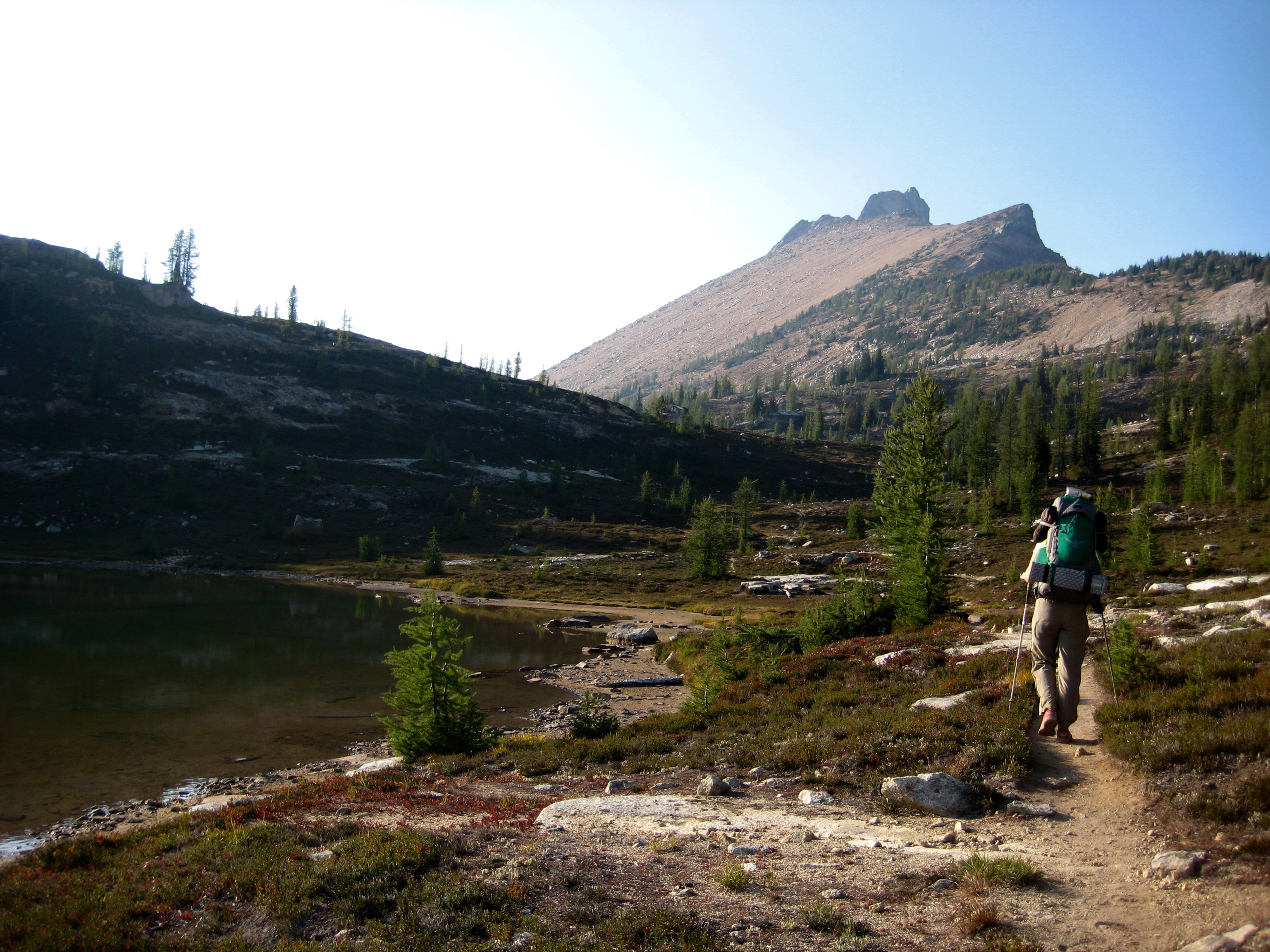 mountain climber hiking passes Lower Snowy Lakes with fall colors and Golden Horn Peak in the distance