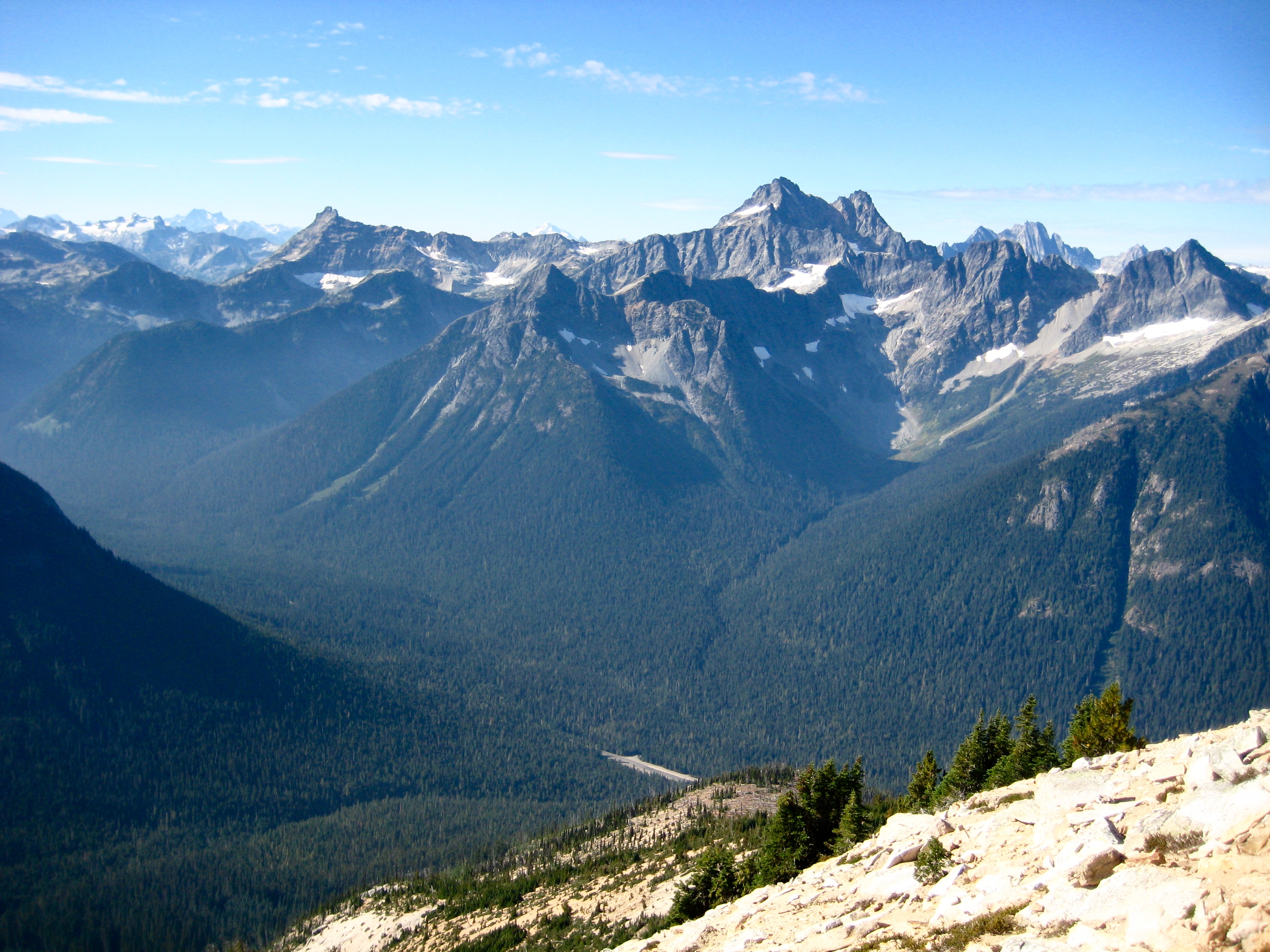 Corteo Peak and Fisher Peak surrounded by other rugged peaks as seen from the summit of Mt Hardy in the Upper Methow Mountains