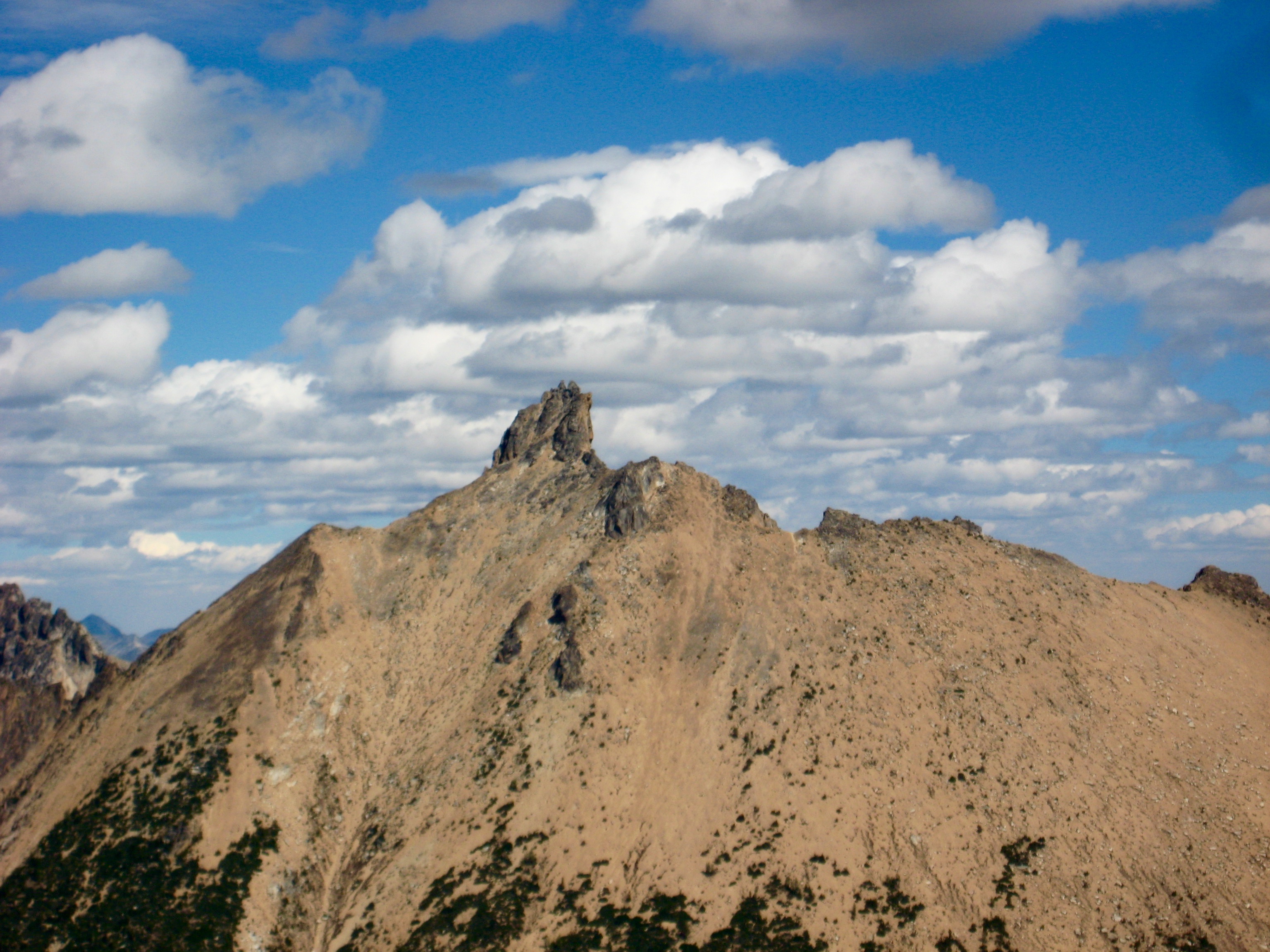 rocky summit horn of Golden Horn peak with puffy clouds as seen from the summit of Mt Hardy in the Upper Methow Mountains