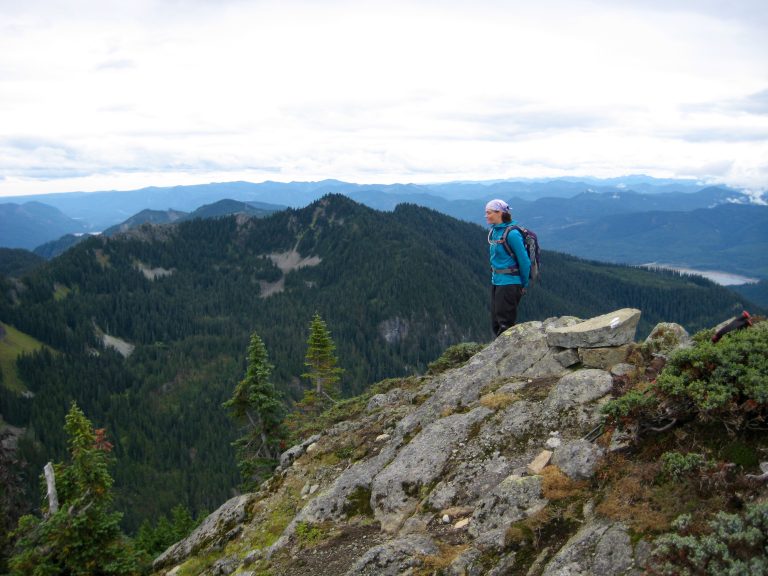 A mountain climber stands on the summit of Dungeon Peak overlooking Lake Keechelus