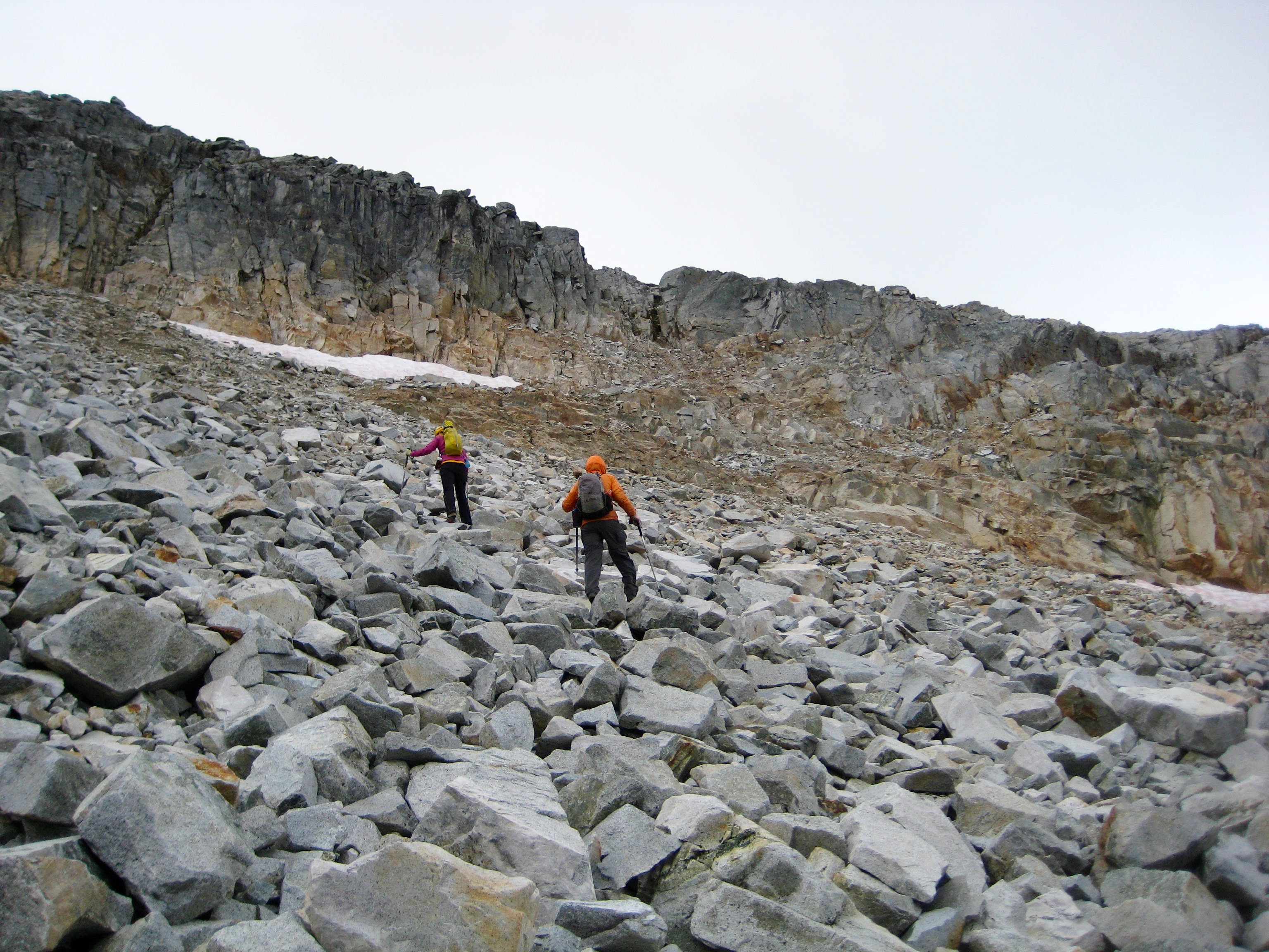 mountain climbers scrambling large boulder field heading for rock ramp which leads up the cliffs of the West Ridge of Bear Mountain in the American Chilliwacks
