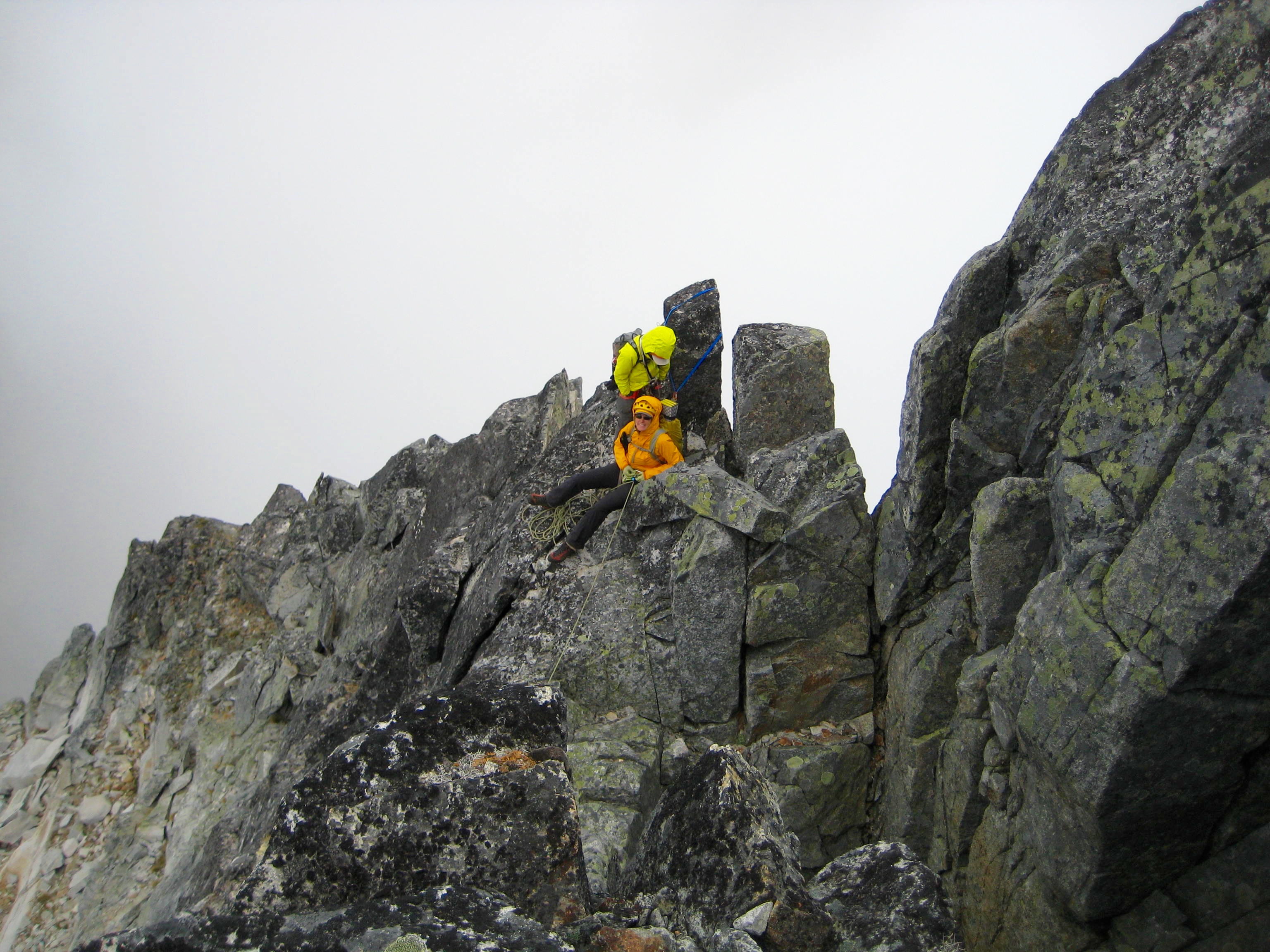 roped mountain climber belaying from rock horns on the steep north ridge near the summit of Bear Mountain of North Cascade National Park