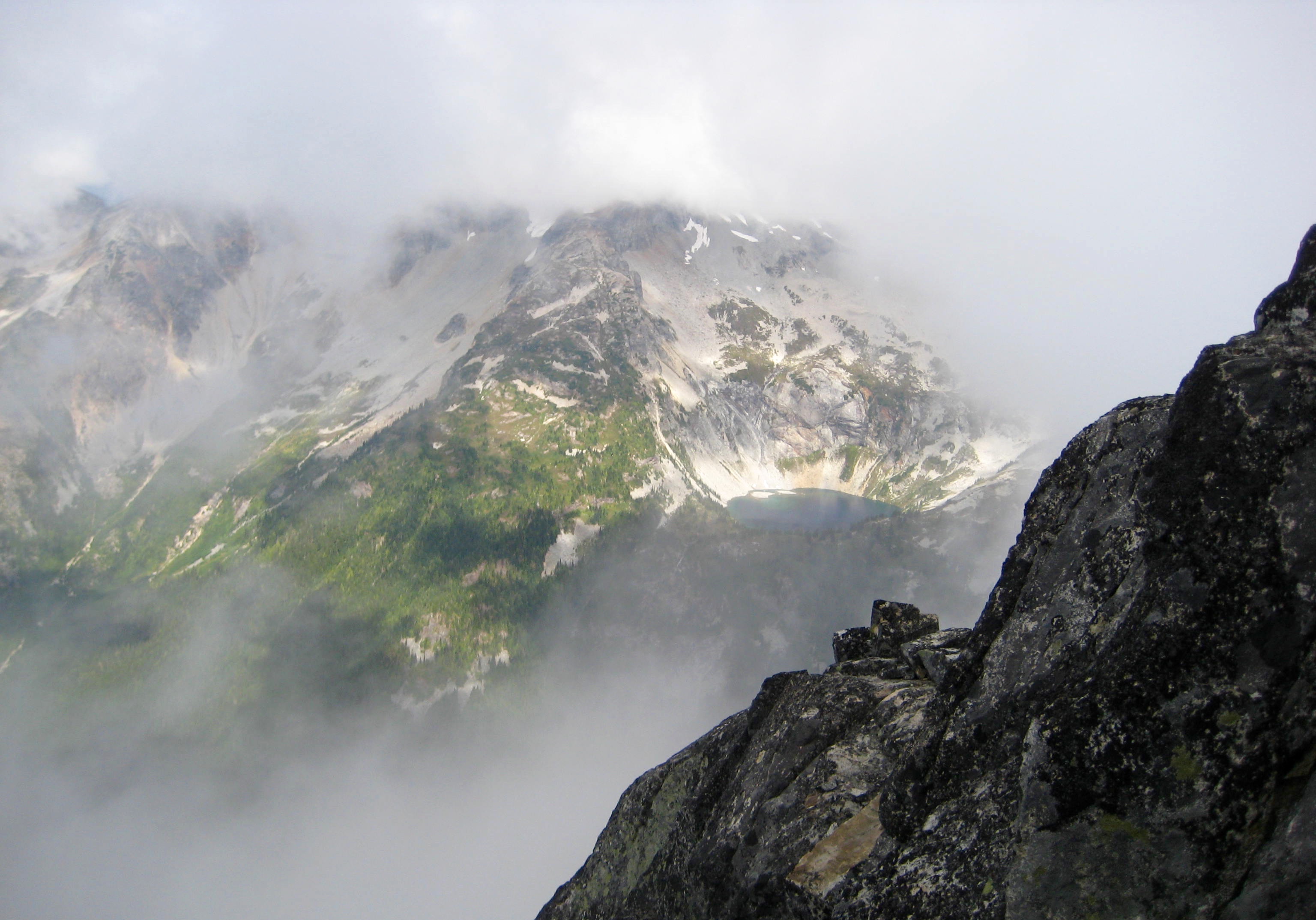 Bear Lake far below the summit of Bear Mountain in the American Chilliwacks in heavy fog with the rocky north ridge of Bear Mountain 