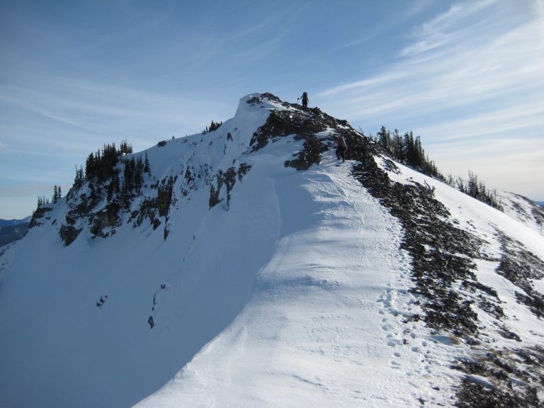 A snowshoer ascends a snowy and rocky ridge crest leading to summit of Norse Peak