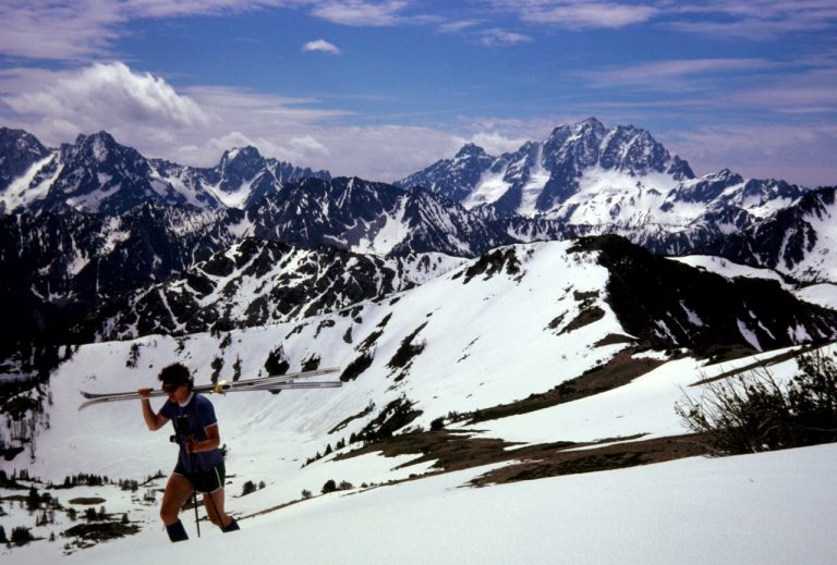 A backcountry skier carries skis up a snowfield on Windy Ridge in the Alpine Lakes Wilderness