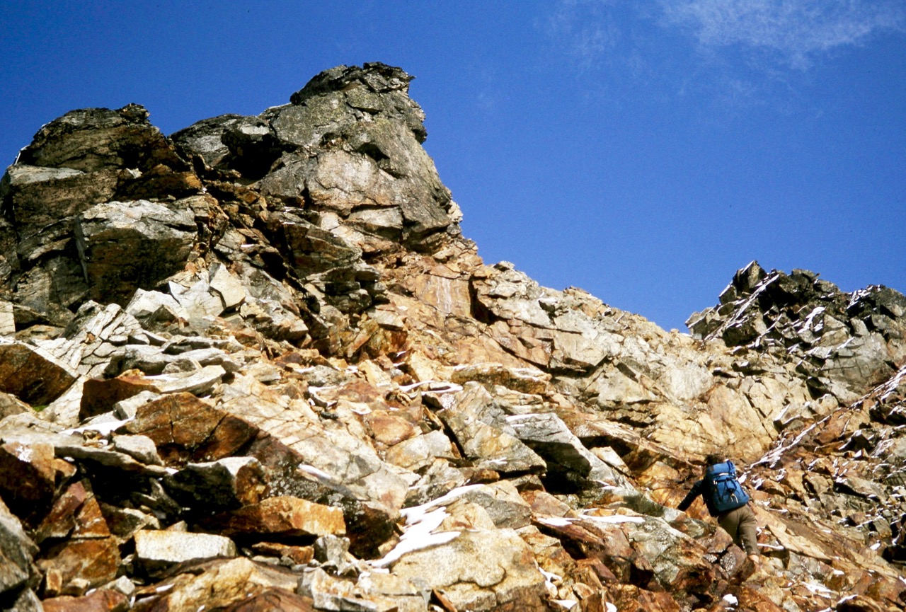 A mountain climber scrambles toward the rocky summit of Sahale Peak