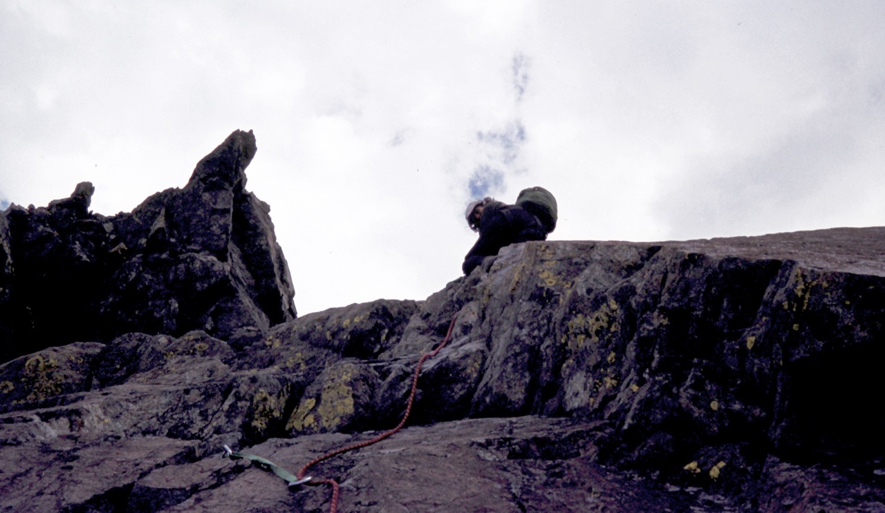 A rock climber scales a steep face of red rock on North Ingalls Peak