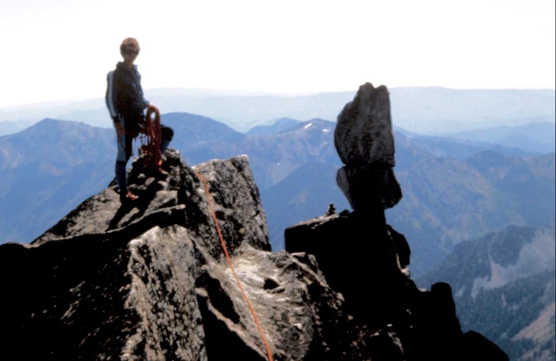 mountain climber on the summit of Sherpa Peak in the Alpine Lakes Wilderness with the balanced rock in the background