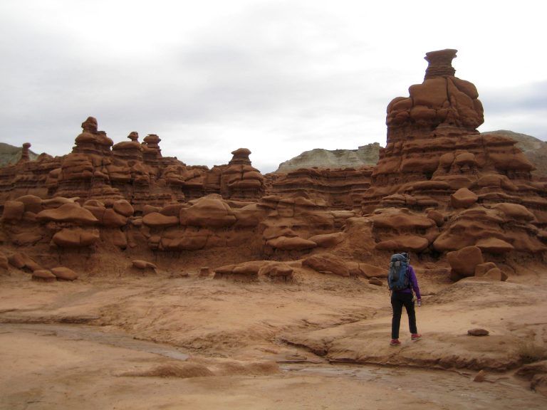 A canyoneer walks through rock formations in Goblin Valley toward Goblins Lair in the San Rafael Swell