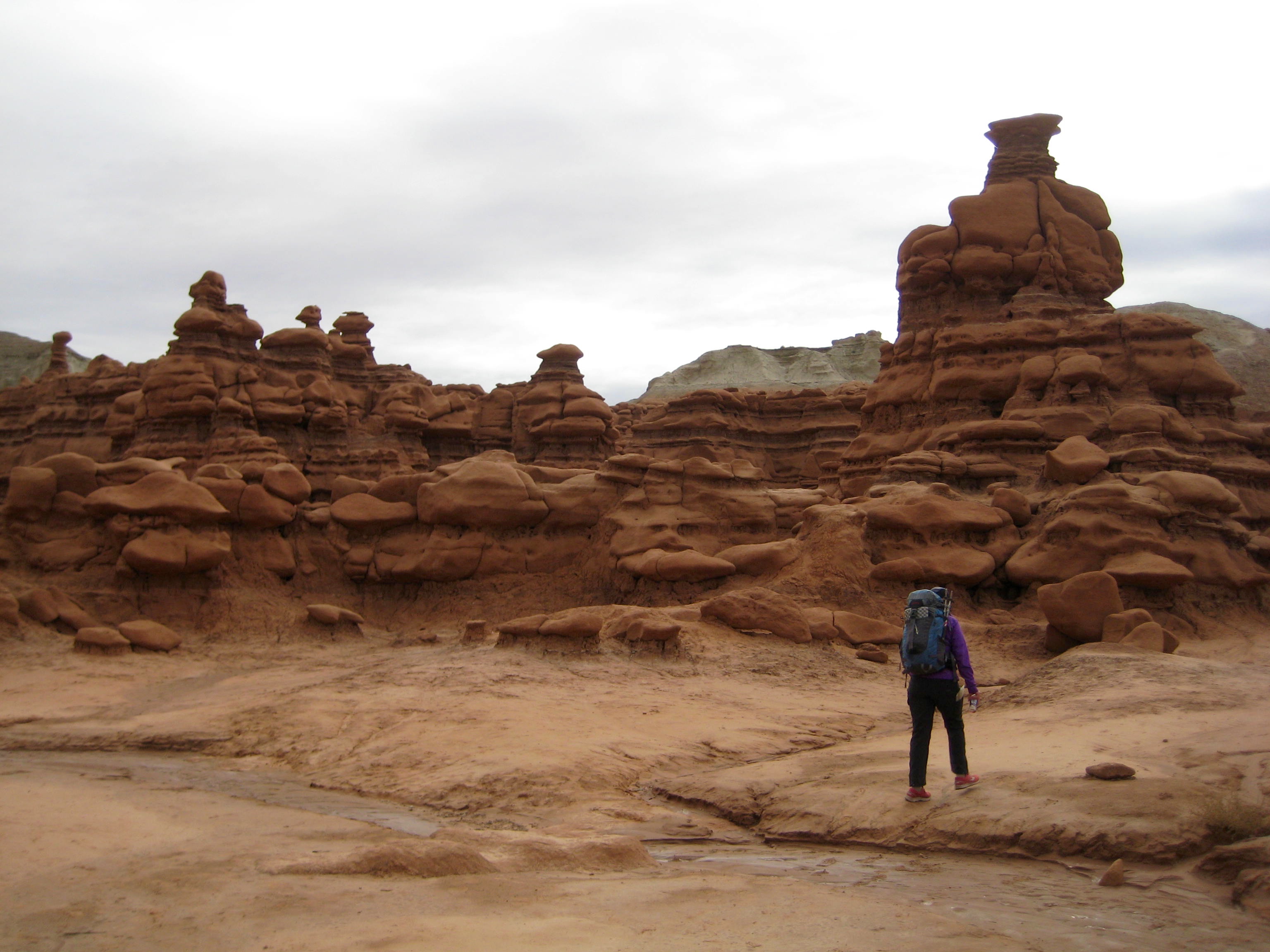 A canyoneer walks through rock formations in Goblin Valley toward Goblins Lair in the San Rafael Swell