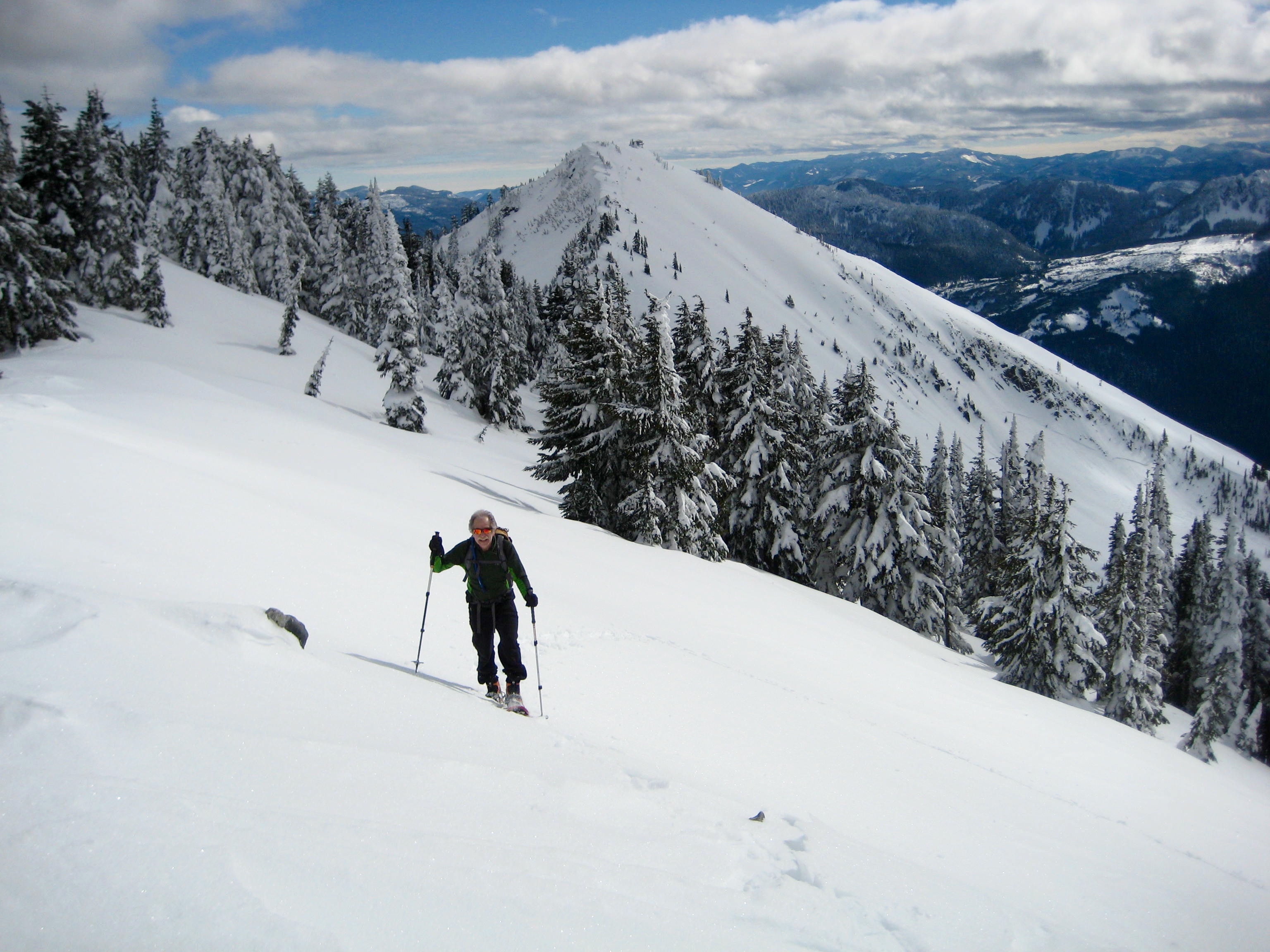 A solo snowshoer ascends an open slope below the summit of West Granite Peak