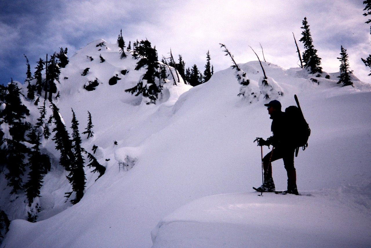 A snowshoe hiker stands on a snowy ridge below Arrowhead Mountain