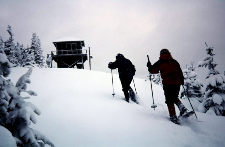Two snowshoers climb a snow slope below the Tolmie Peak lookout cabin