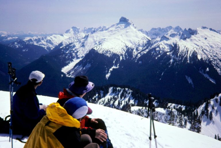 Snowshoers on summit of Breccia Peak look over at lofty Sloan Peak