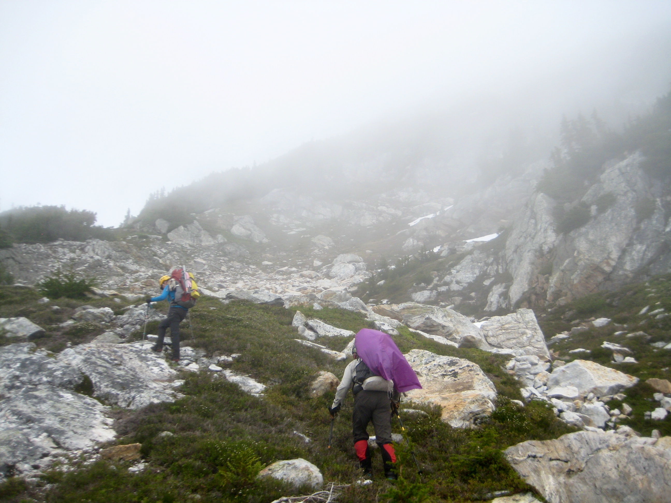 mountain climbers ascending heather and rock slabs with fog on Isolation Peak in the North Cascades