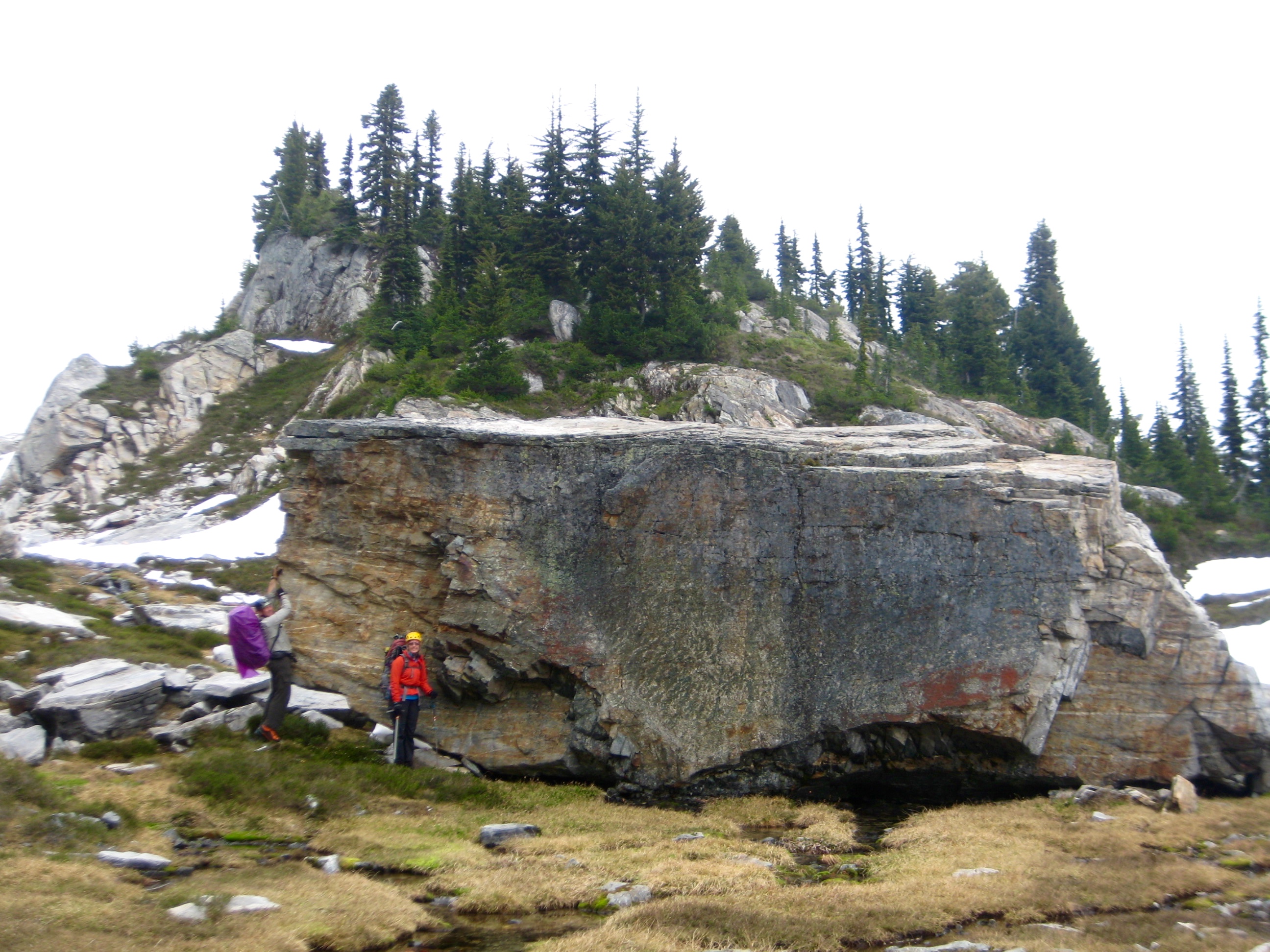 mountain climbers stand next to an enormous Schist Monolith in a heather meadow along the Isolation Traverse in the North Cascades