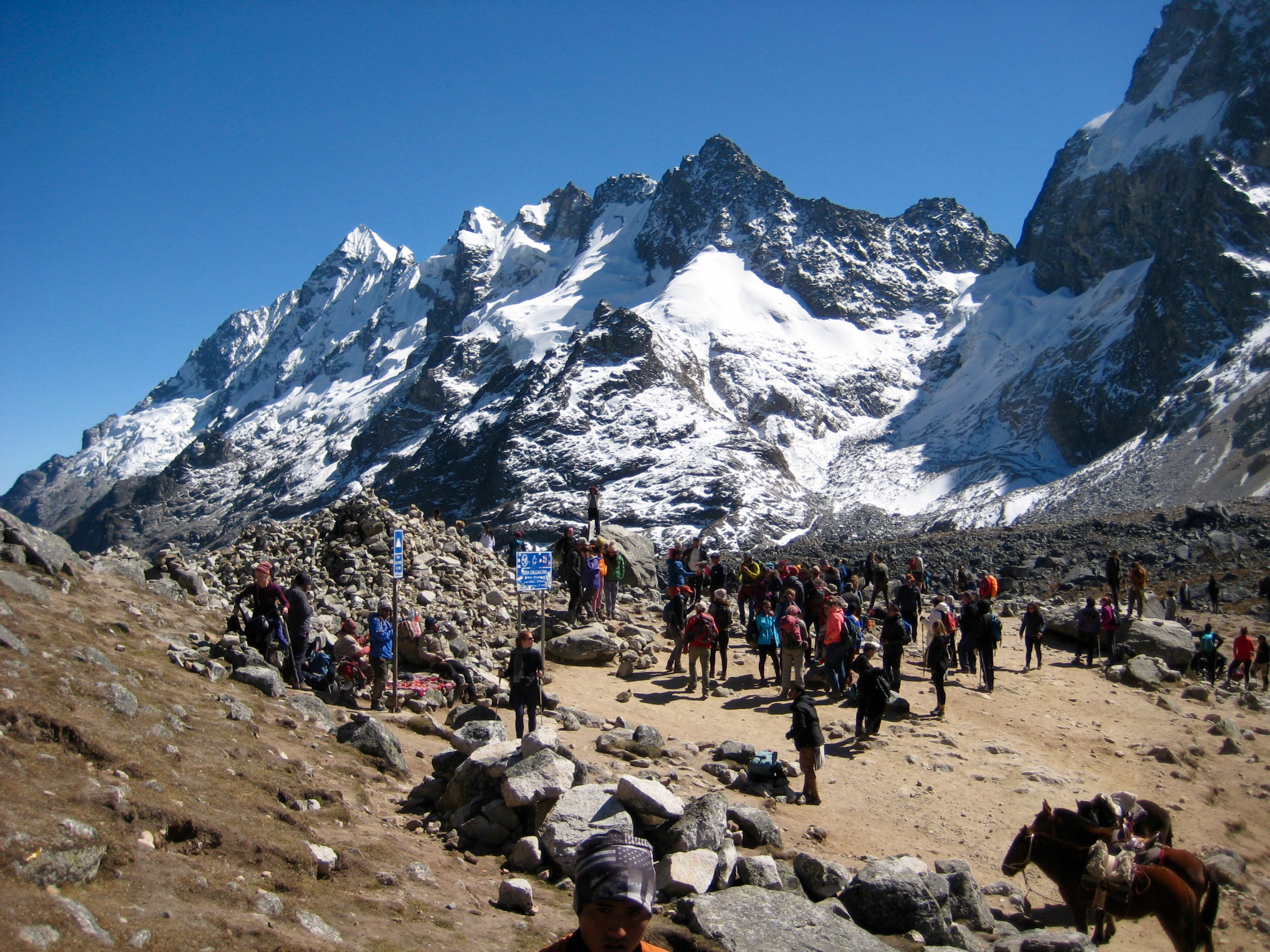 big crowds of trekkers at Salkantay Pass with snow covered mountains