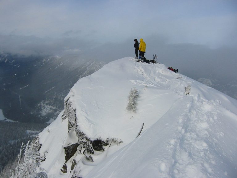 Three snowshoers stand atop a snowy Red Mountain