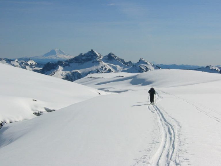 A backcountry skier glides along a snowy ridge below Cowlitz Rocks