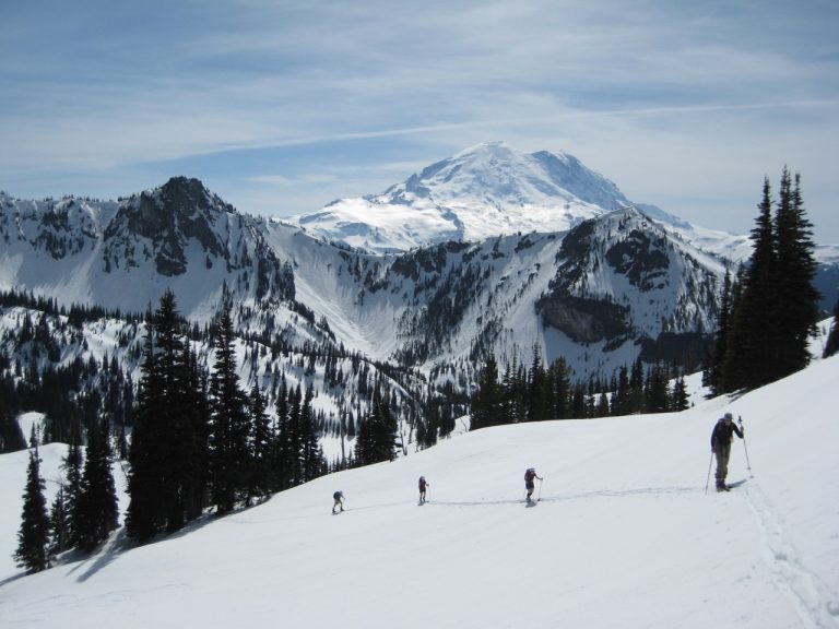 Four backcountry skiers ascend from snowy Crystal Bowl with Mt Rainier behind