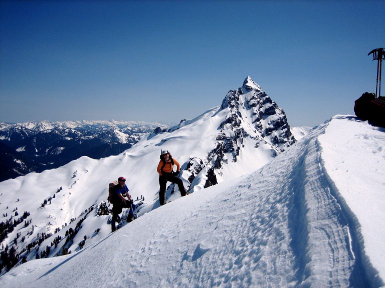 Two snowshoers approach the summit of Bedal Peak with Sloan Peak behind