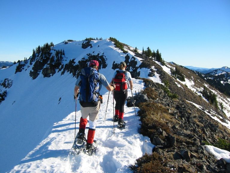 Two snowshoers hike up a broad snowy ridge toward Norse Peak