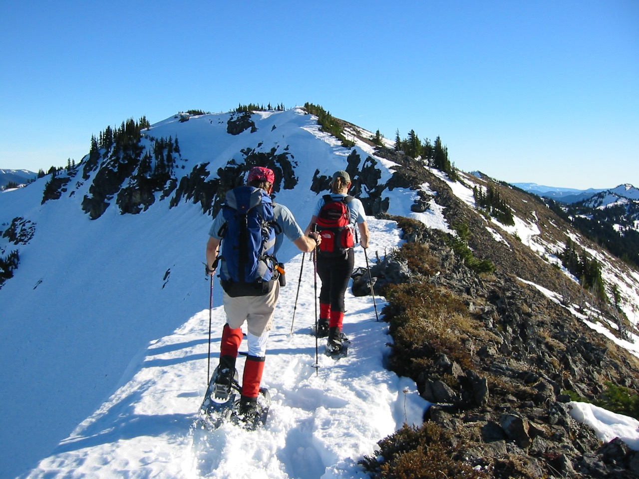 Two snowshoers hike up a broad snowy ridge toward Norse Peak