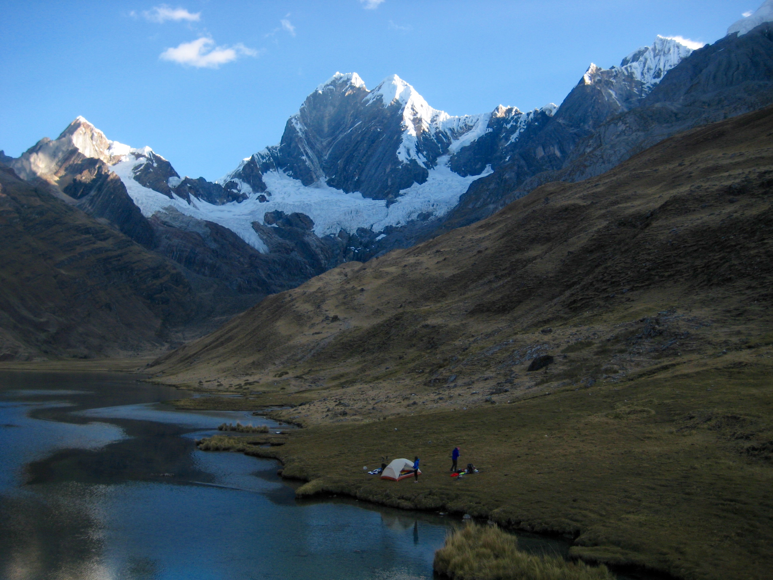 Nevado Jirishanca stands above Lake Mitucocha with grassy tundra and a backpackers camp on the Huayhaush Circuit