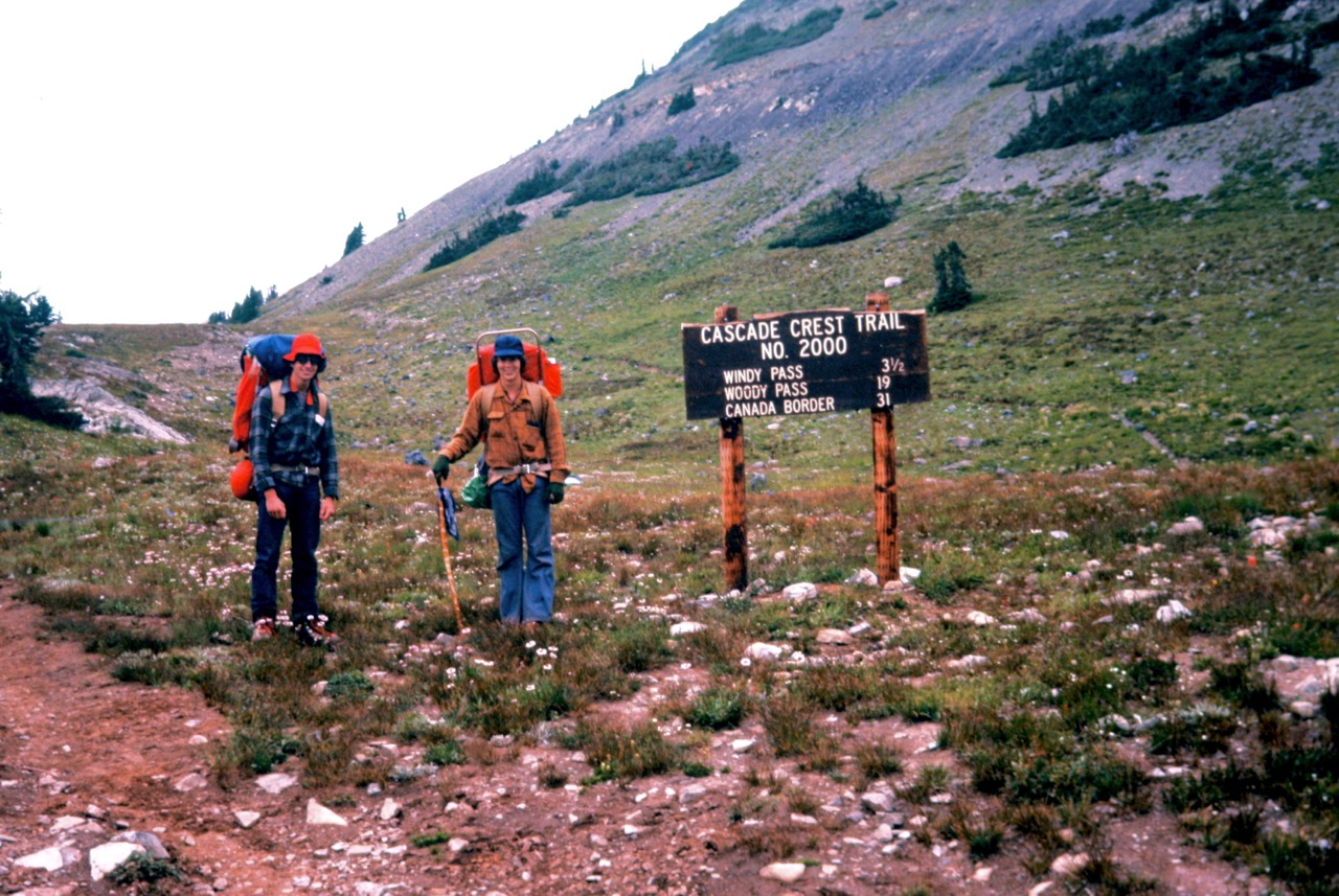 Two young backpackers stand at a trailhead sign near Harts Pass after hiking a portion of the Pacific Crest Trail in Washington